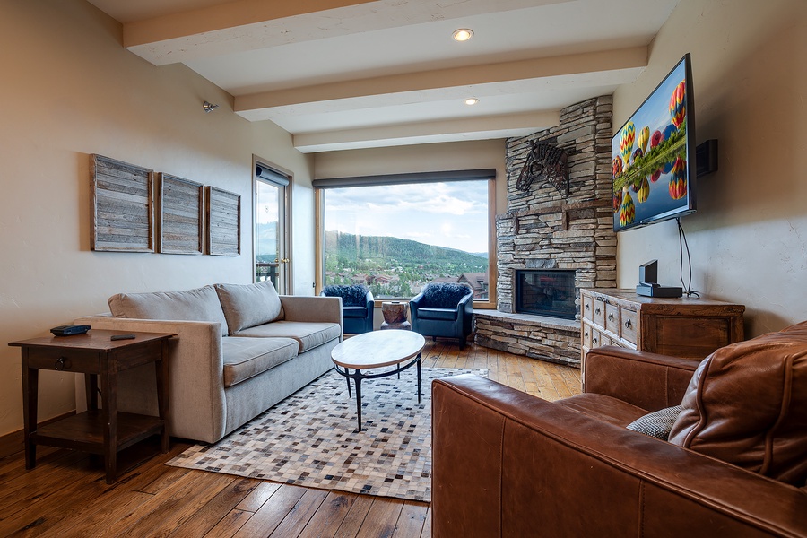 Unwind in your spacious living room where a stone fireplace adds warmth and floor-to-ceiling windows frame breathtaking mountain views—your perfect retreat after exploring the area.