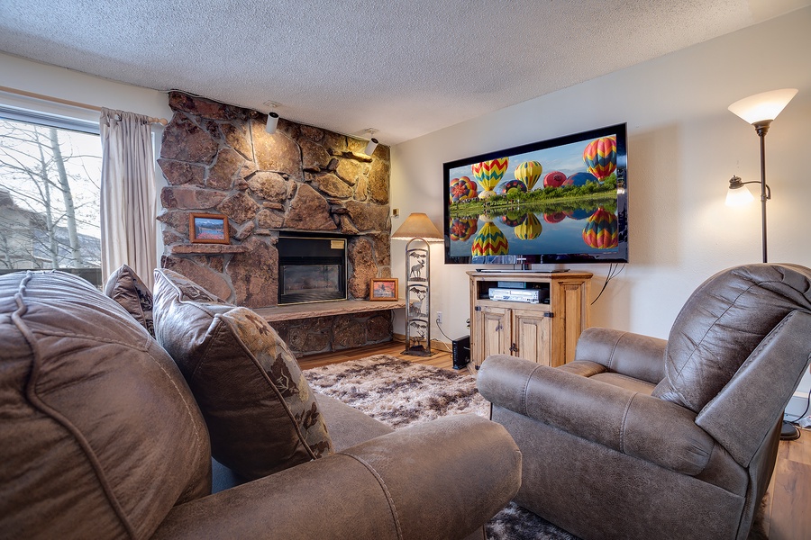 Unwind in your cozy living room with plush seating, a warm stone fireplace, and entertainment at your fingertips—perfect for relaxing after a day of adventure.