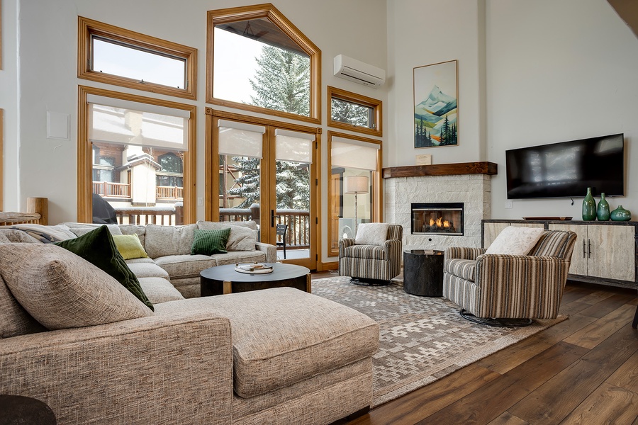 Unwind in your sunlit living room where soaring windows frame alpine views, a cozy fireplace crackles nearby, and plush seating invites you to relax after a mountain adventure.