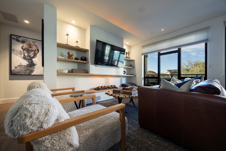 Sink into plush leather and cozy textures in this modern living room, where open shelving displays personal touches and floor-to-ceiling windows frame sweeping views of the surrounding landscape. Your perfect retreat awaits.