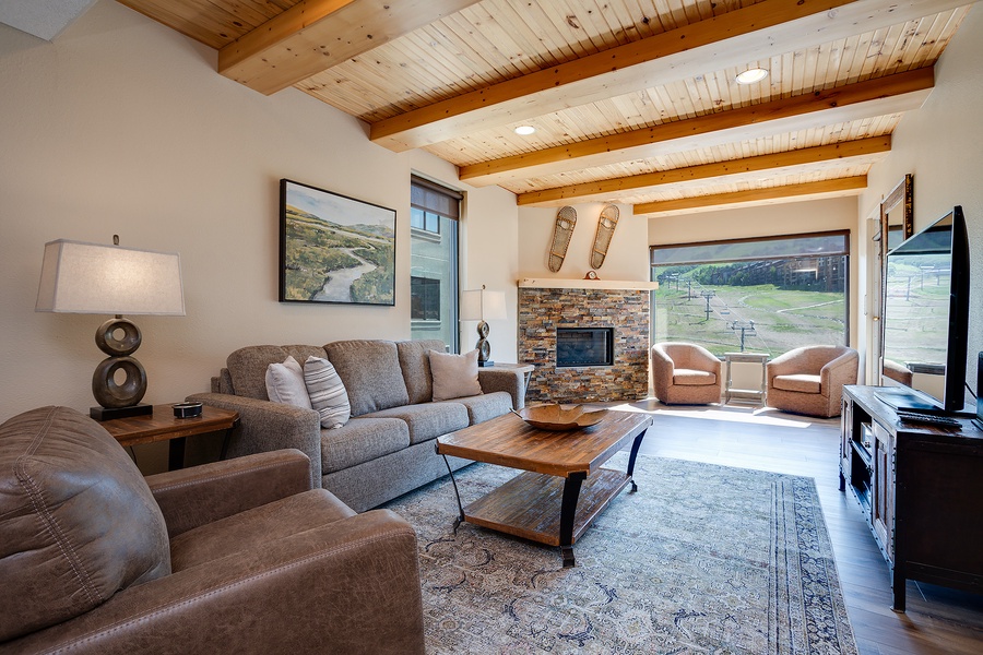 Step into your cozy living room with vaulted wood-beam ceilings, a stone fireplace, and sweeping mountain views—your perfect retreat after a day of adventure.