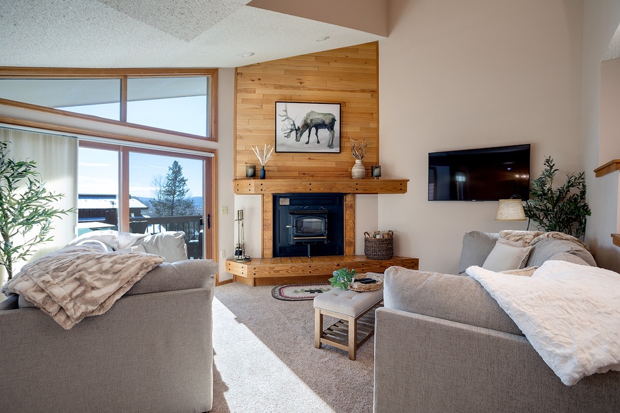 Unwind in your bright living room with plush sofas, a warm fireplace, and serene lake views through soaring windows—your perfect mountain retreat for cozy evenings together.
