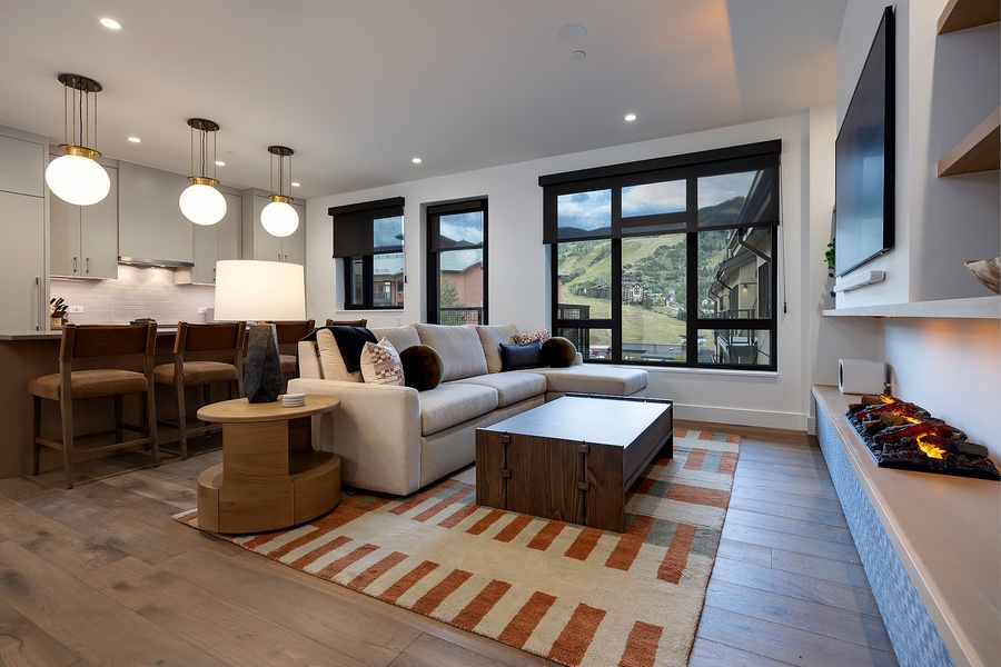 Sink into the plush sectional and drink in sweeping mountain views through floor-to-ceiling windows. Modern pendant lights and a cozy fireplace create your perfect alpine retreat.
