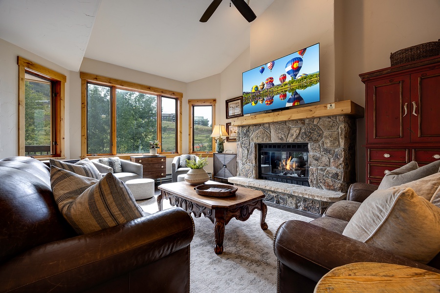 Sink into plush seating beside a crackling stone fireplace, surrounded by vaulted ceilings and sweeping natural light—your cozy retreat awaits.