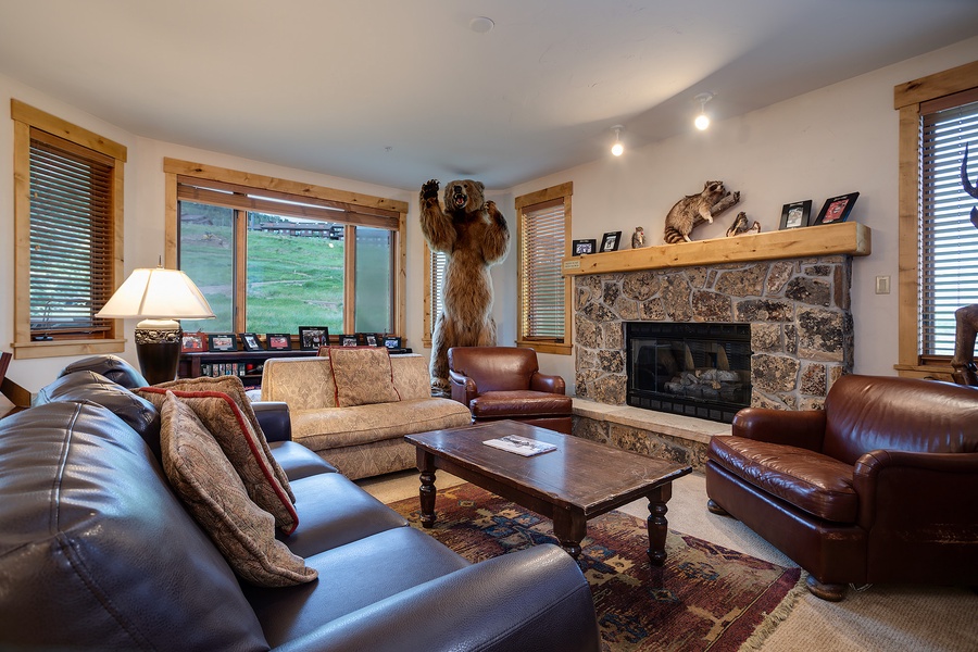 Gather around the stone fireplace in this inviting living room, where rustic charm meets comfort. Large windows frame mountain views while leather seating and warm wood tones create your perfect retreat.