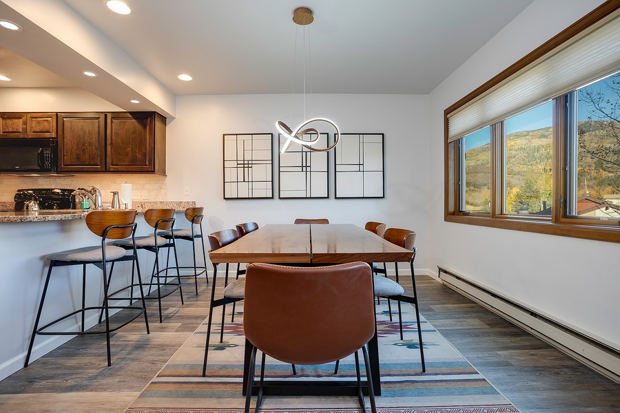 Your open-concept kitchen and dining area invites you to gather around the modern table with stunning mountain views through wide windows, perfect for morning coffee or evening meals together.