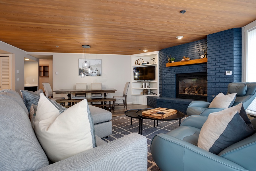 Unwind in your spacious living area with a stunning fireplace, warm wood-paneled ceiling, and cozy seating where you can relax after a day of adventure.