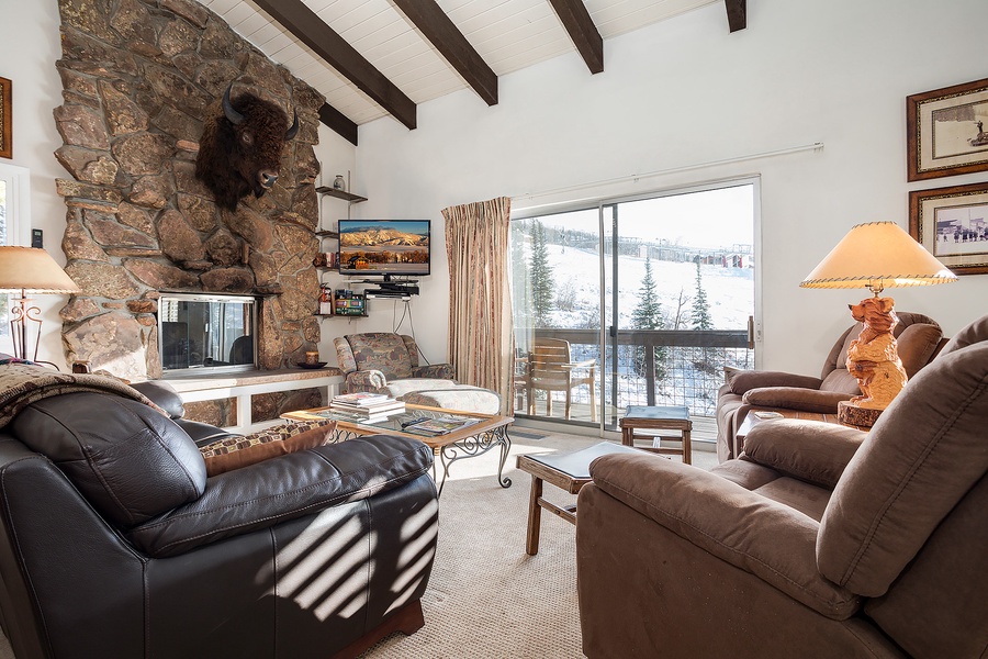 Cozy up in your mountain retreat with soaring beamed ceilings, a striking stone fireplace, and plush seating overlooking snowy slopes—pure alpine comfort awaits.