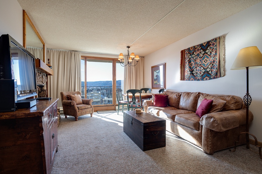Sink into your spacious living room featuring a plush leather sofa, rich wood furnishings, and southwestern décor. Natural light floods through your private balcony doors, framing stunning mountain vistas that invite you to unwind in style.