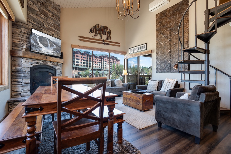 Your mountain retreat features soaring ceilings, rustic stone fireplace, and plush seating that invites you to unwind. Large windows frame stunning views, while the spiral staircase adds a charming loft touch.