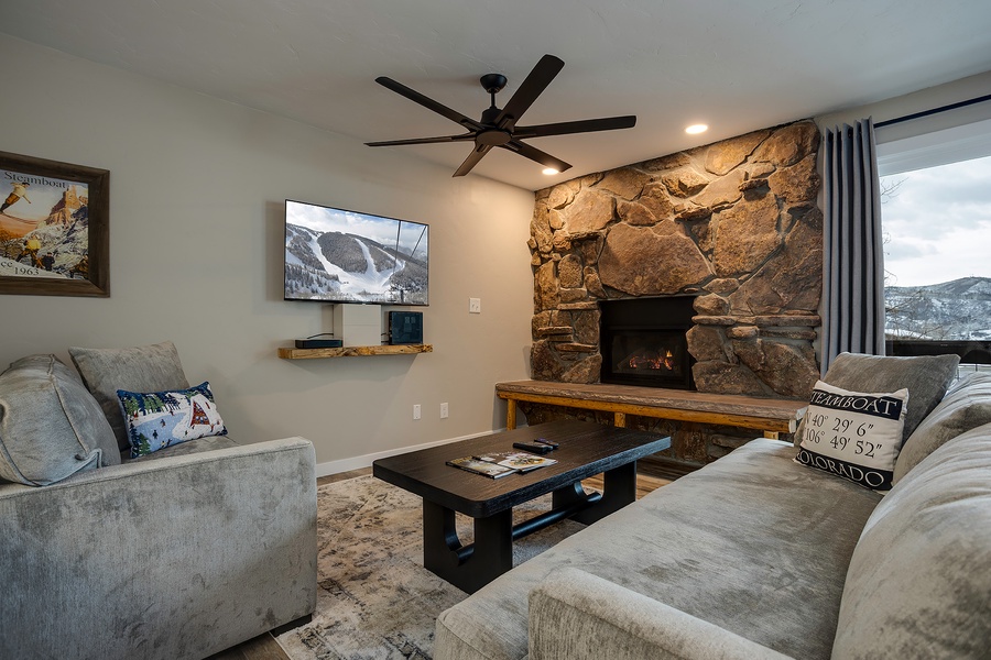 Sink into plush seating and watch the fire glow against the dramatic stone hearth, while mountain views stretch beyond your windows.