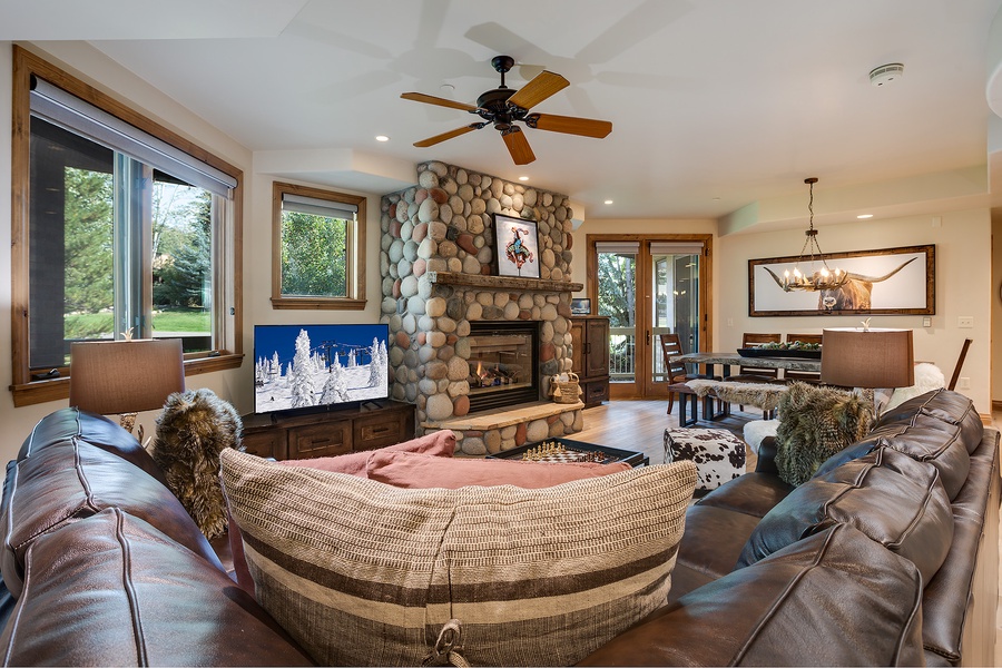 Sink into plush leather seating beside a warm river-rock fireplace. Your open-concept retreat features natural wood accents, high ceilings, and views of the outdoors—perfect for relaxing after a day of adventure.