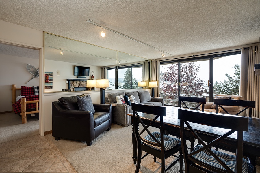 Relax in your open-concept living and dining area, where cozy seating, a warm fireplace, and stunning lake views through floor-to-ceiling windows create the perfect retreat for memorable evenings.