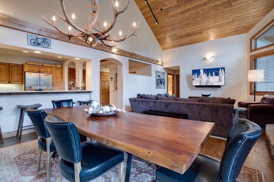 Gather around the handsome wood table under a stunning antler chandelier, where high ceilings and warm wood accents create a cozy yet spacious retreat for your group.