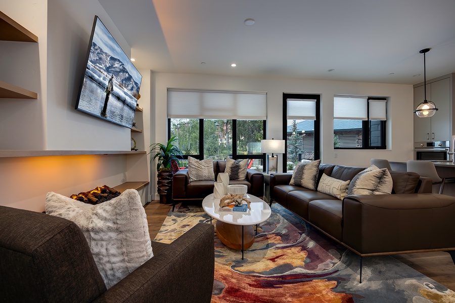 Sink into plush leather sofas and unwind by the glowing fireplace—your perfect retreat after a day of adventure. Sunlight streams through tall windows, bathing the open living space in warmth.