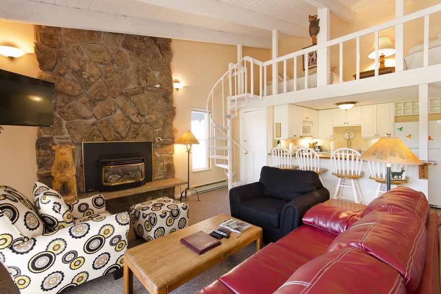 Cozy living area featuring a dramatic stone fireplace, comfortable seating, and a unique spiral staircase leading to your private loft-style sleeping area—perfect for mountain getaway memories.
