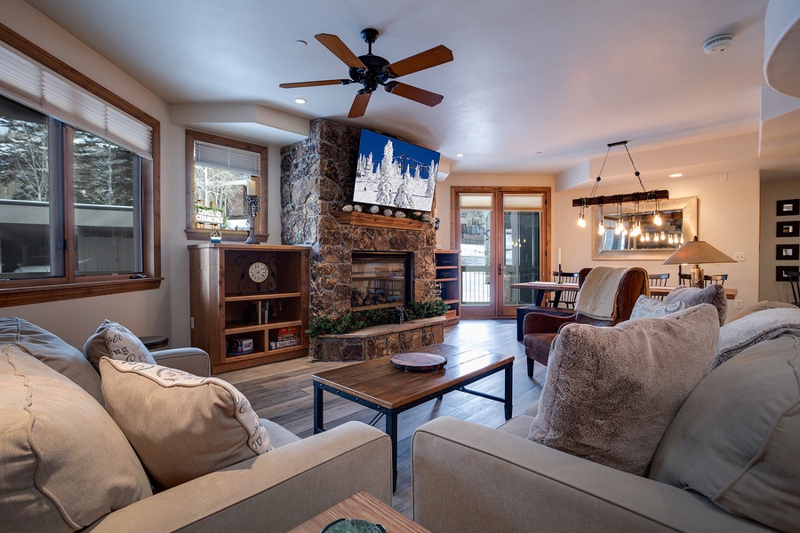 Unwind in your inviting living room with plush seating, a stunning stone fireplace, and natural light streaming through large windows. Your perfect mountain retreat awaits.
