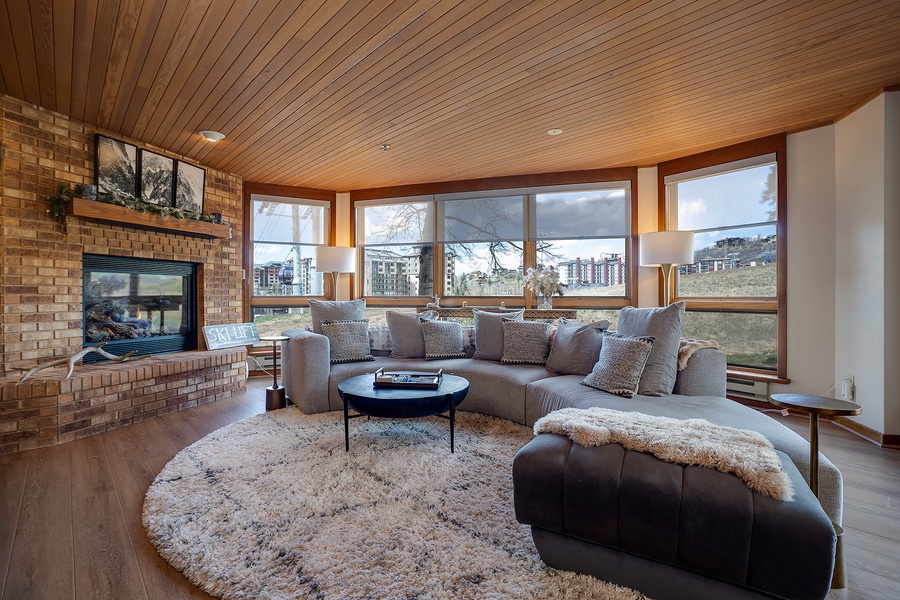 Curl up by the warmth of your fireplace in this inviting living room, where panoramic windows frame stunning views and plush seating invites you to unwind in style.