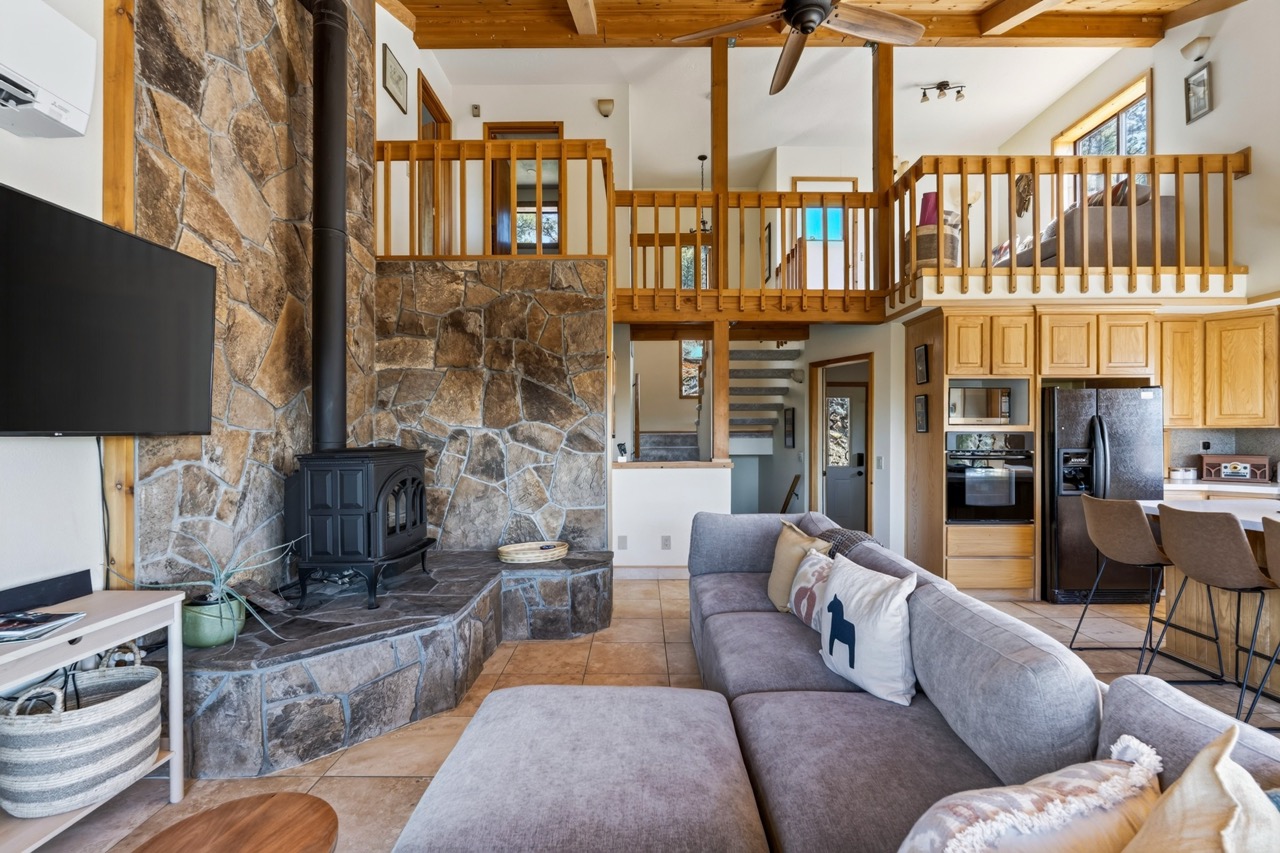 Relax in this inviting open-concept living space with soaring wood-beamed ceilings, a striking stone fireplace, and cozy seating that invites you to unwind in mountain-chalet style.