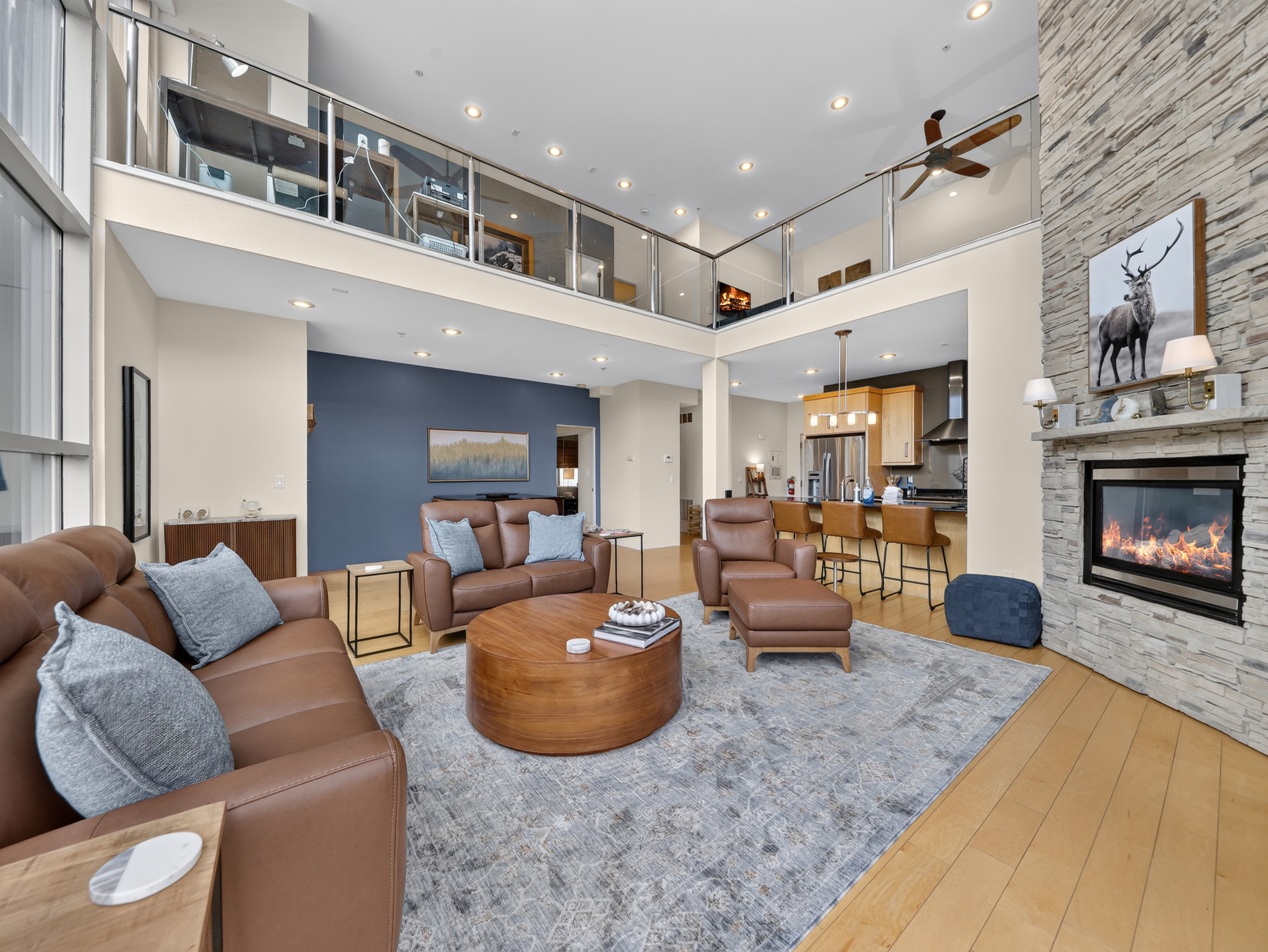 Gather around the glowing fireplace in your spacious two-story living area, where natural light pours through soaring windows and a loft-style layout creates an open, airy feel perfect for group gatherings.