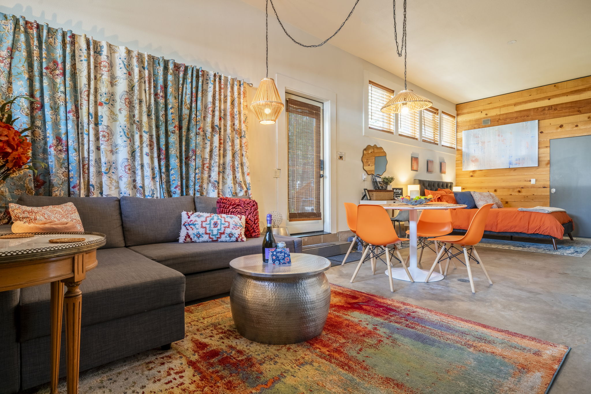 Your open-plan retreat blends vibrant living, dining, and sleeping spaces with warm wood accents, woven pendant lights, and colorful textiles—a cozy, eclectic haven for relaxation.