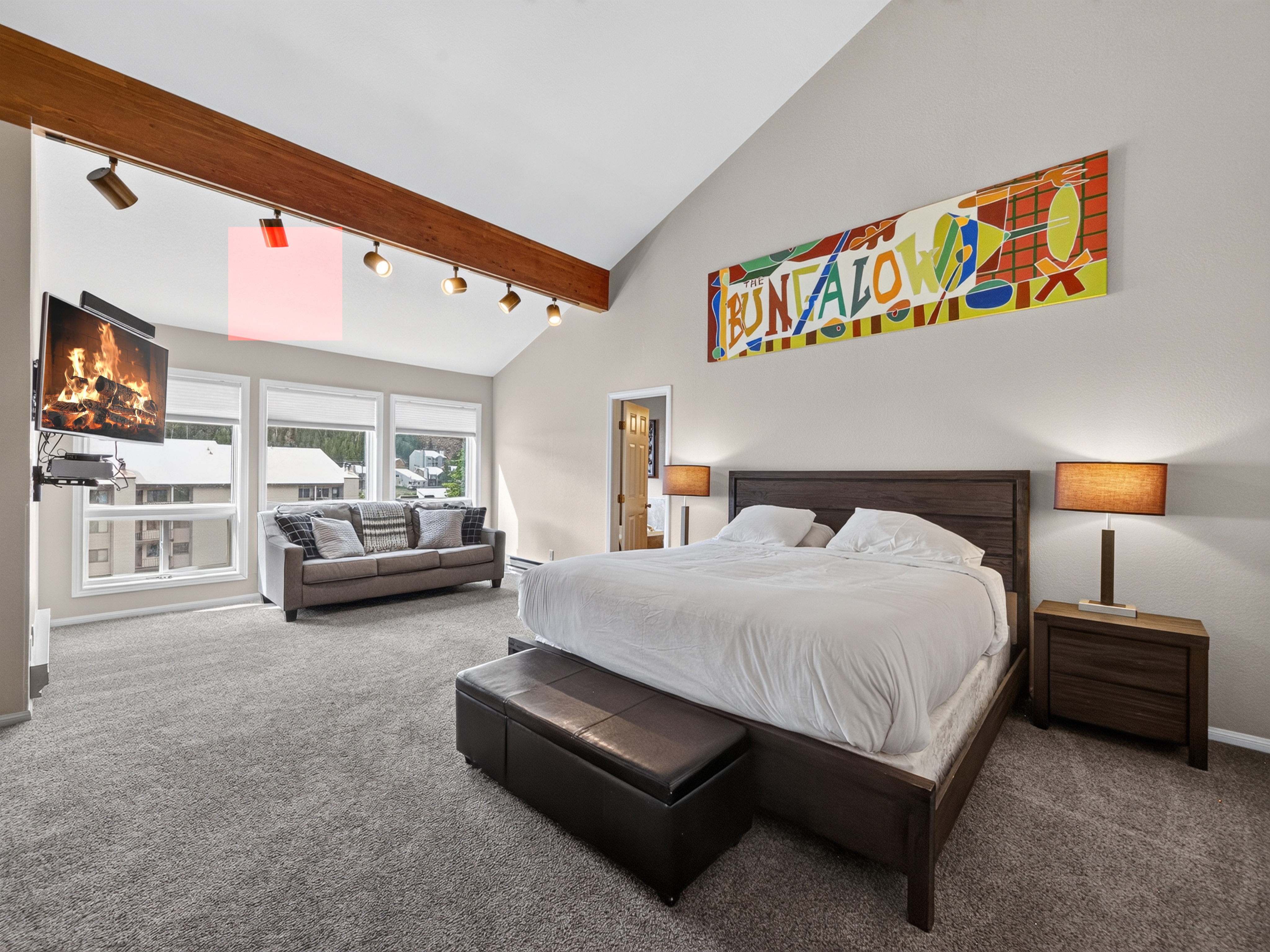 Sink into the plush bed under vaulted ceilings with a cozy fireplace and sunlit windows. The warm wood beams and vibrant art set the tone for your perfect retreat.