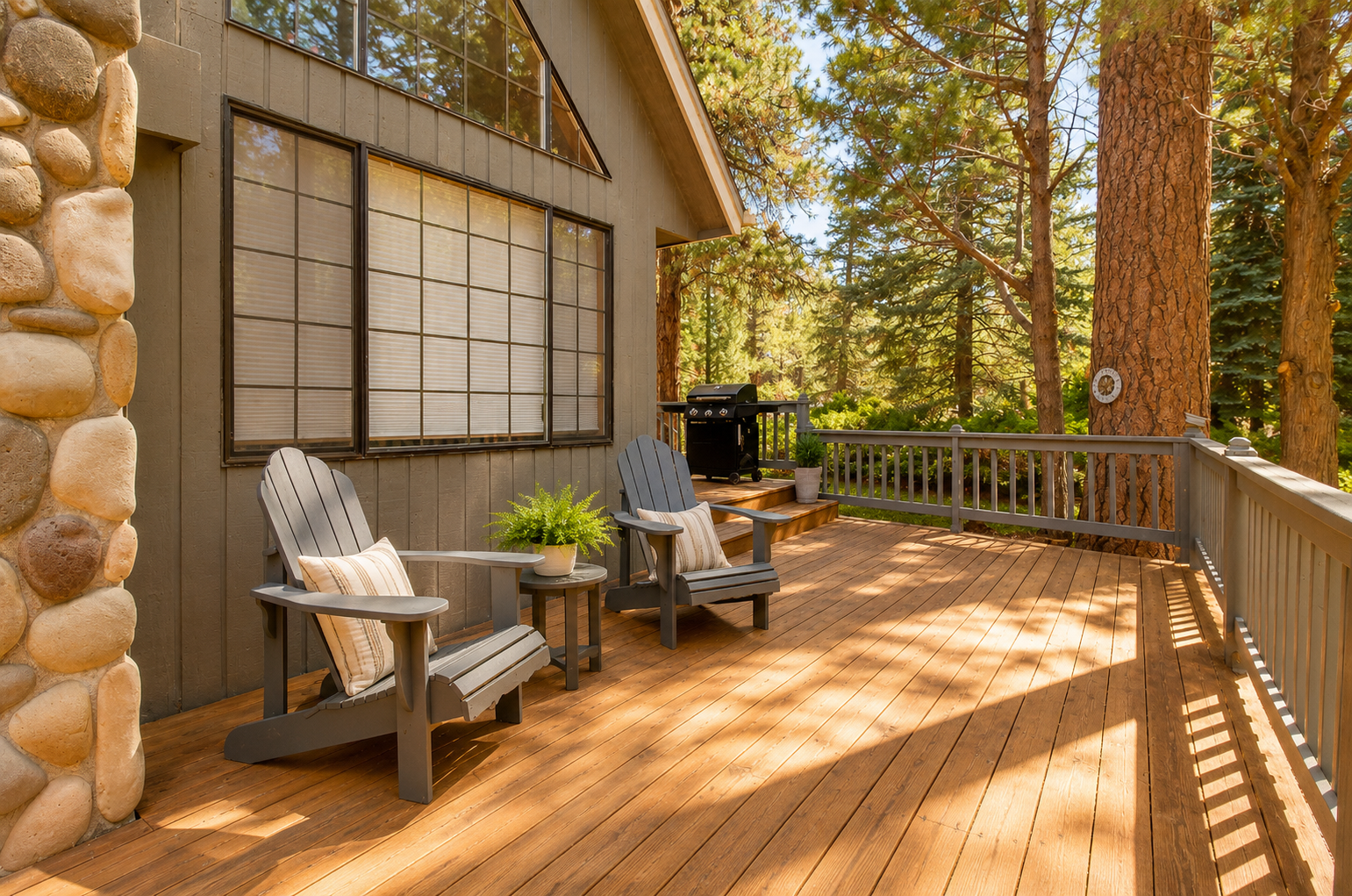 Sunlit deck with cozy Adirondack chairs and BBQ, where your mornings start with coffee among towering pines and peaceful forest views.