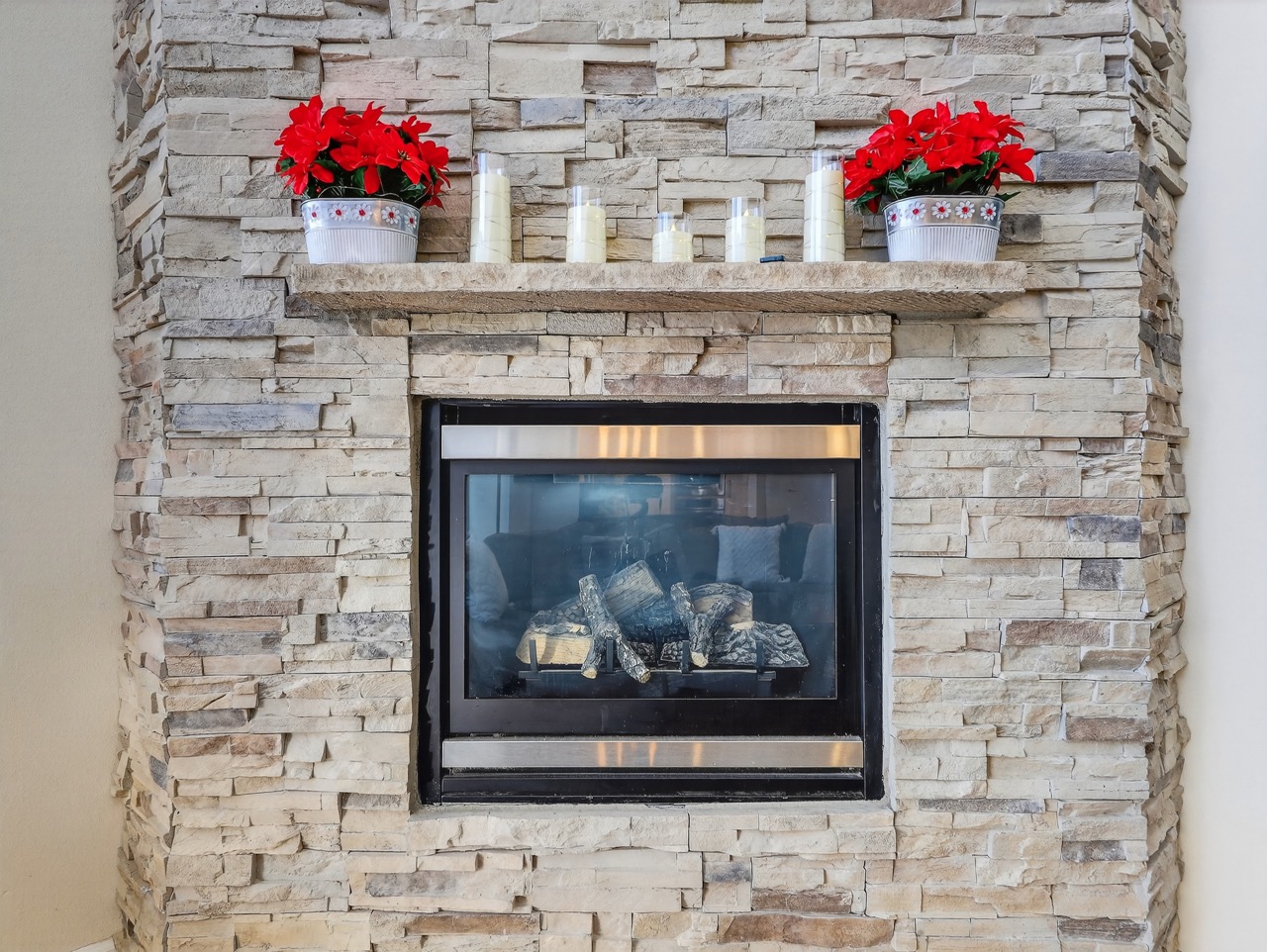 Cozy up by your elegant stone fireplace, where flickering flames and festive red blooms create the perfect ambiance for relaxing evenings.