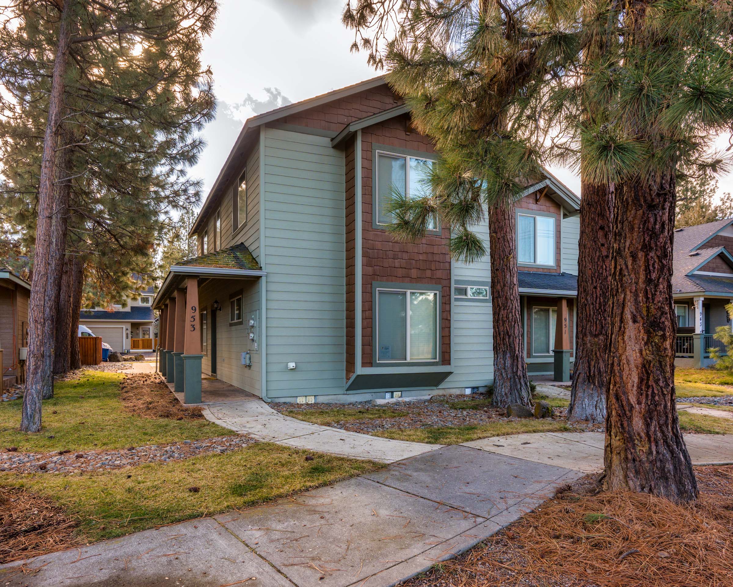 A modern two-story rental home nestled among towering pine trees in a peaceful residential neighborhood.