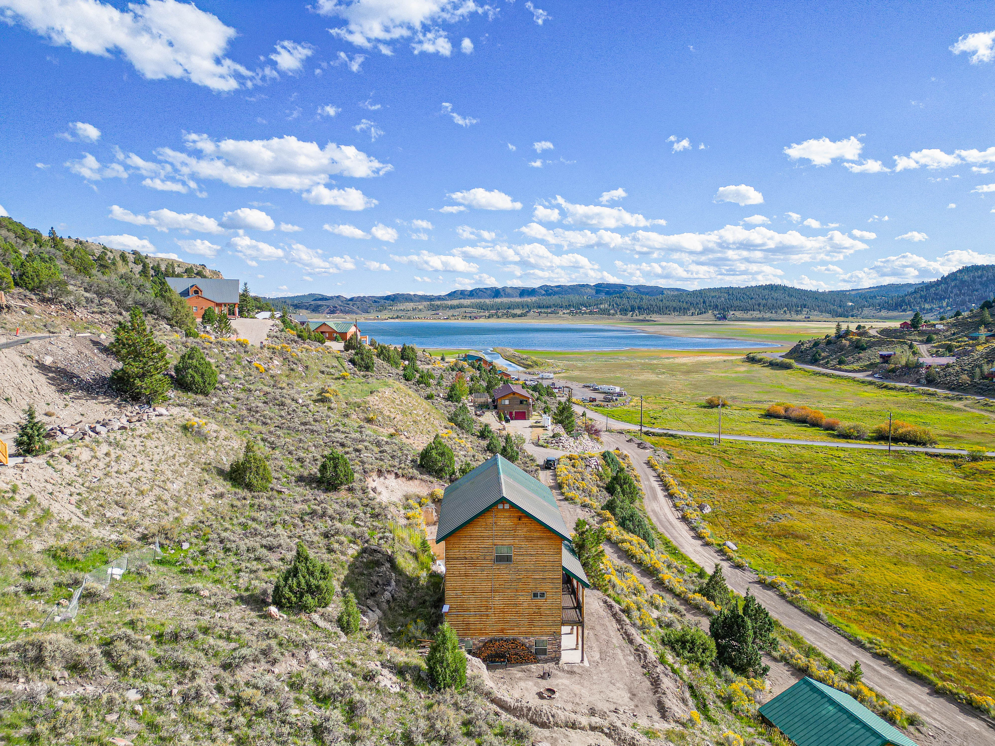 Aerial view of a vacation home nestled on a hillside, surrounded by natural landscape with lake and mountain scenery in the distance.