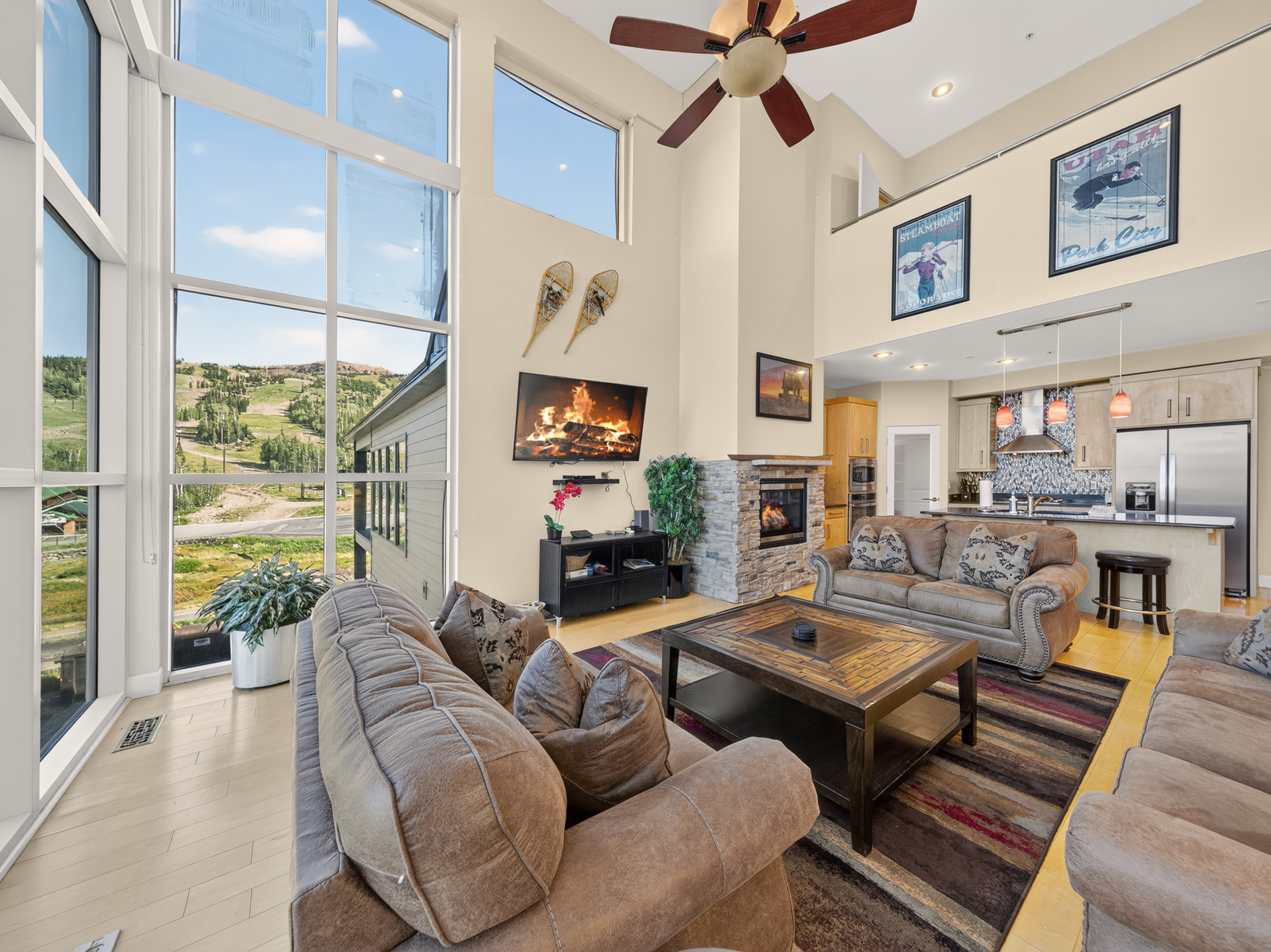 Sink into plush sofas beneath soaring ceilings as natural light streams through floor-to-ceiling windows, revealing mountain vistas. Your cozy fireplace and open kitchen await—perfect for gathering and unwinding together.