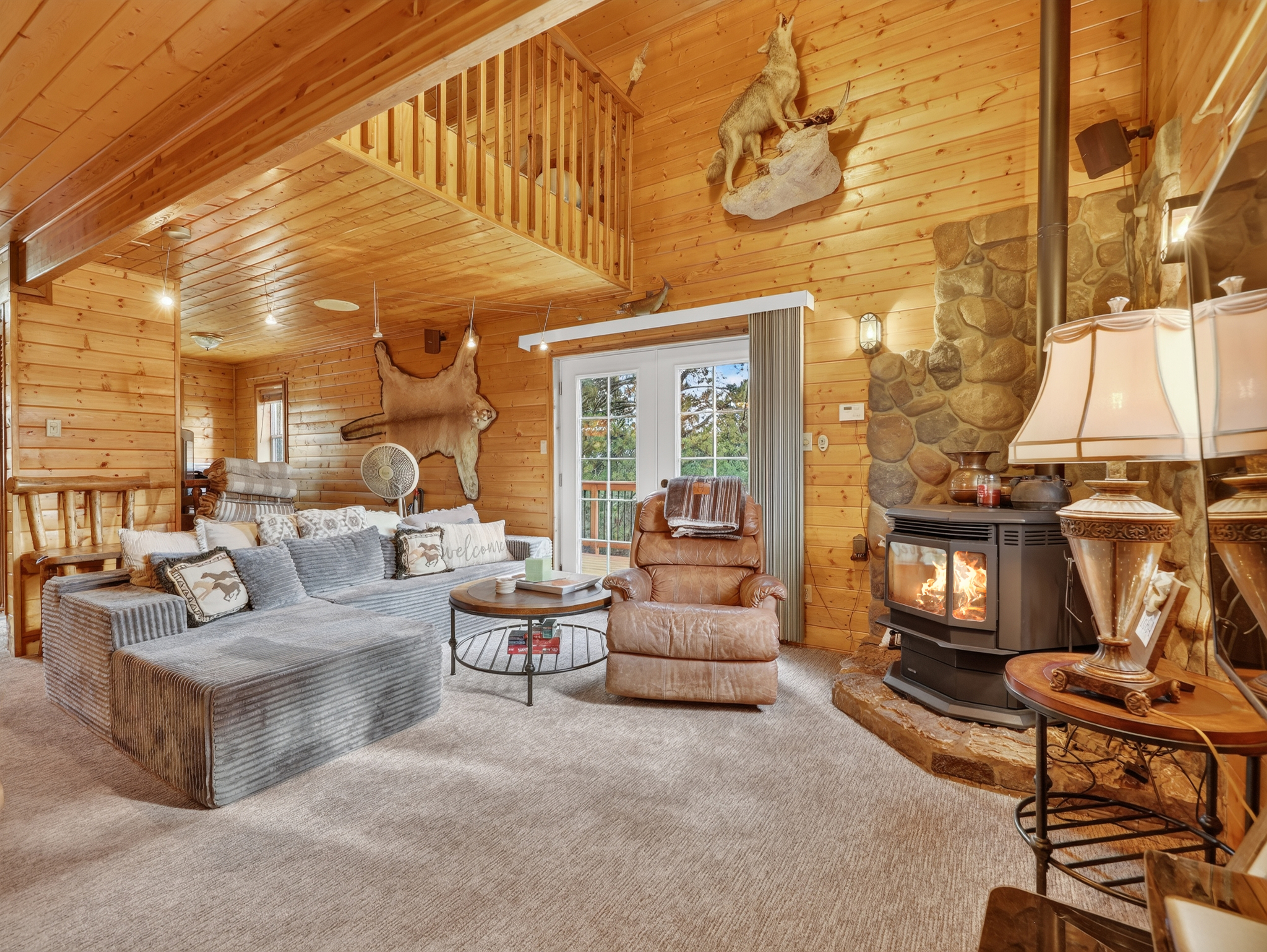 Warm up in your rustic living room with exposed pine, a crackling fireplace, and a cozy loft above. Natural light streams through French doors, inviting you to relax on plush seating.