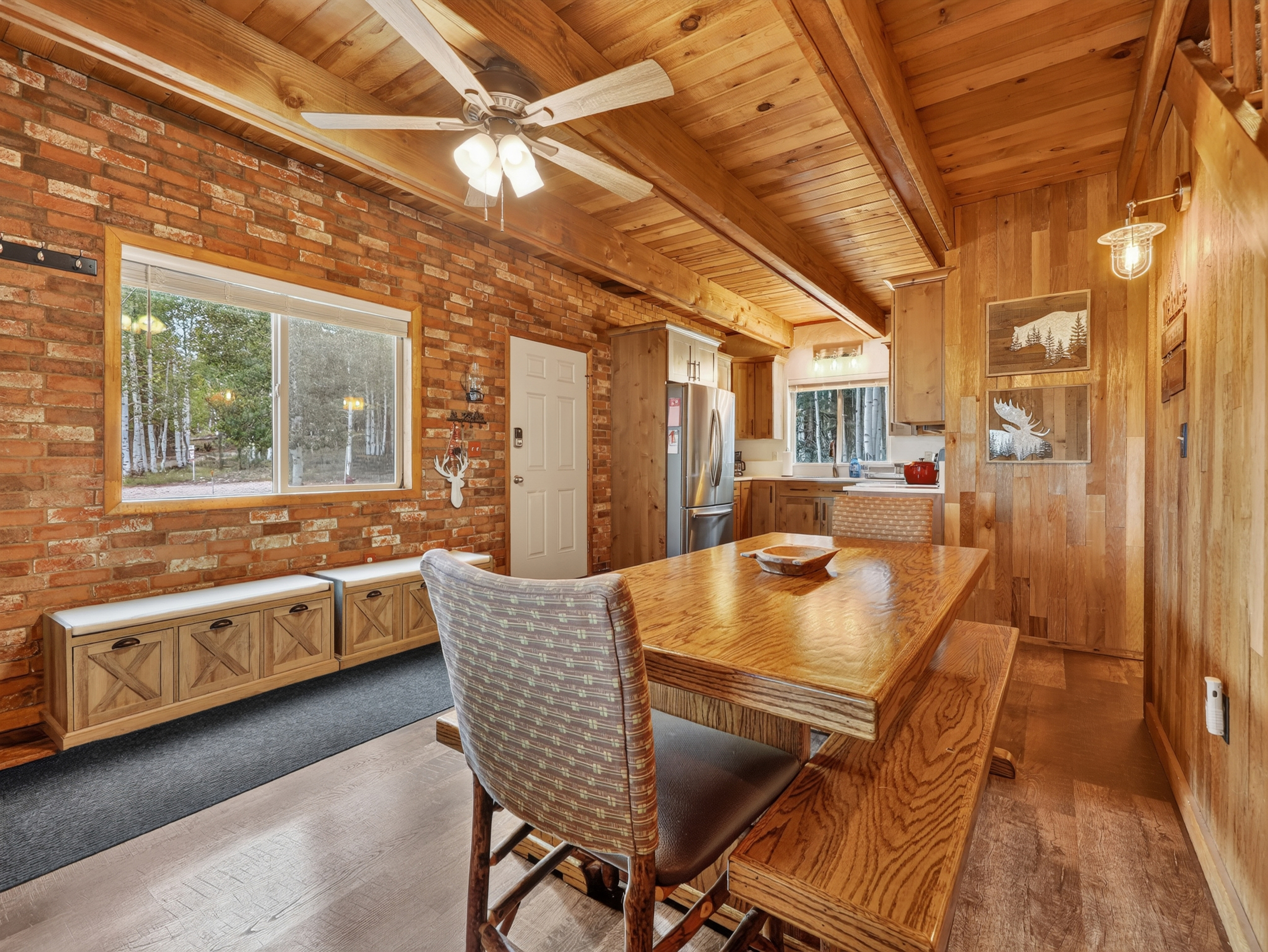 Gather around your handcrafted wood dining table under soaring vaulted ceilings, where rustic brick walls meet warm cabin charm and forest views peek through every window.