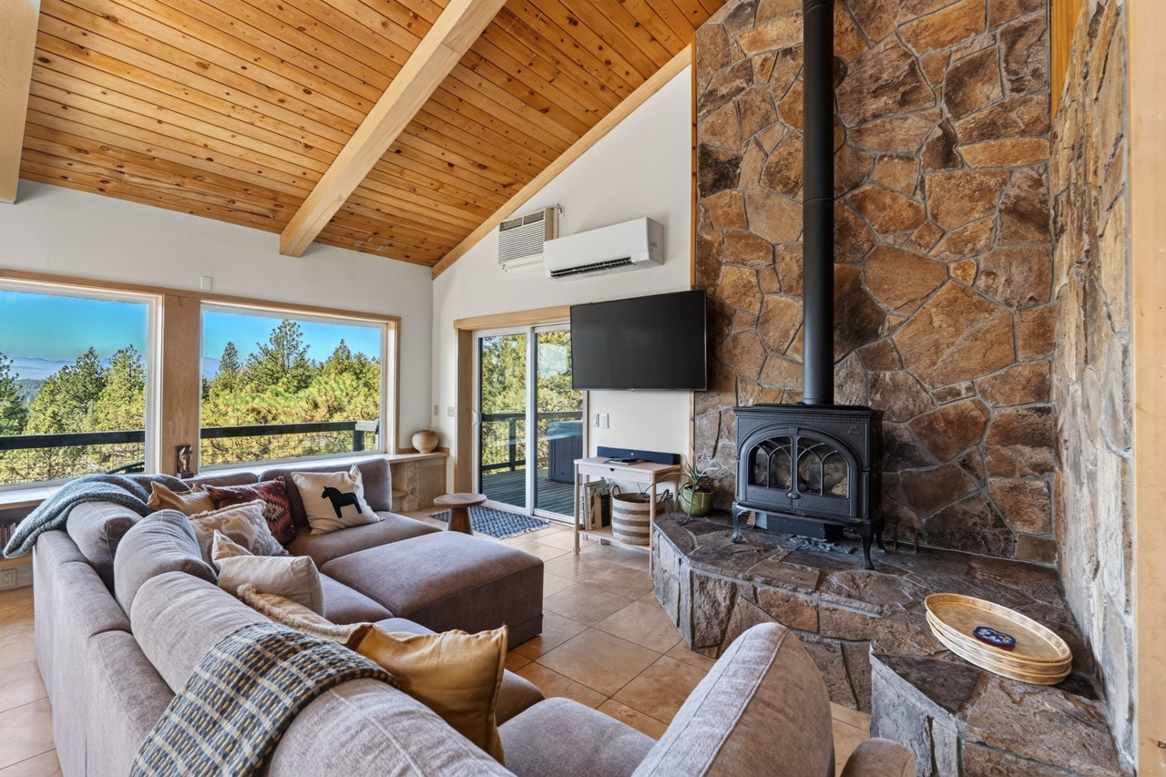 Settle into your cozy living room where vaulted wood ceilings and a stunning stone fireplace create the perfect mountain retreat. Through expansive windows, you'll enjoy natural light and peaceful views of the surrounding pines.