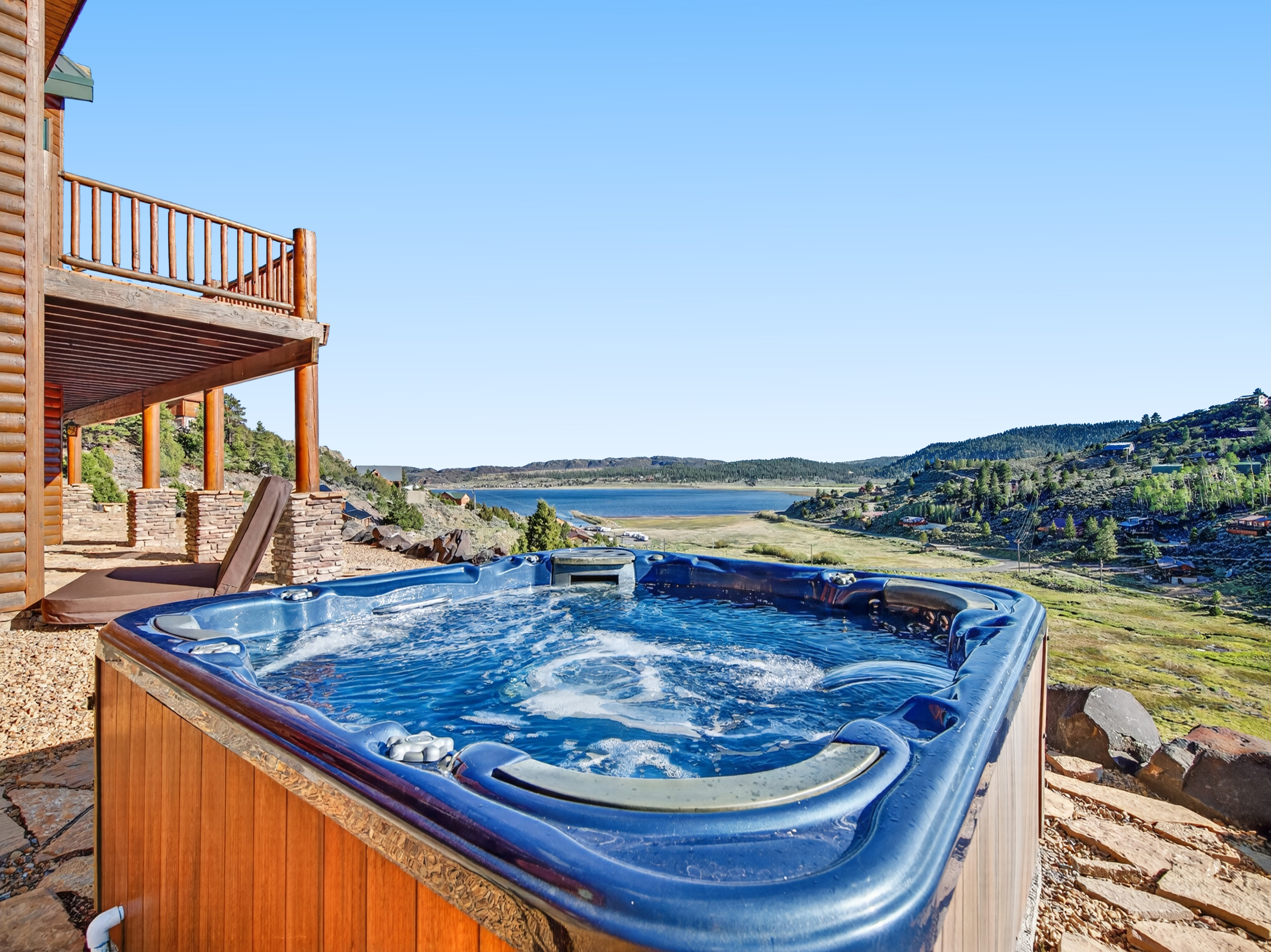 Soak in the hot tub while overlooking a stunning lake and mountain landscape, perfect for unwinding after a day of adventure.