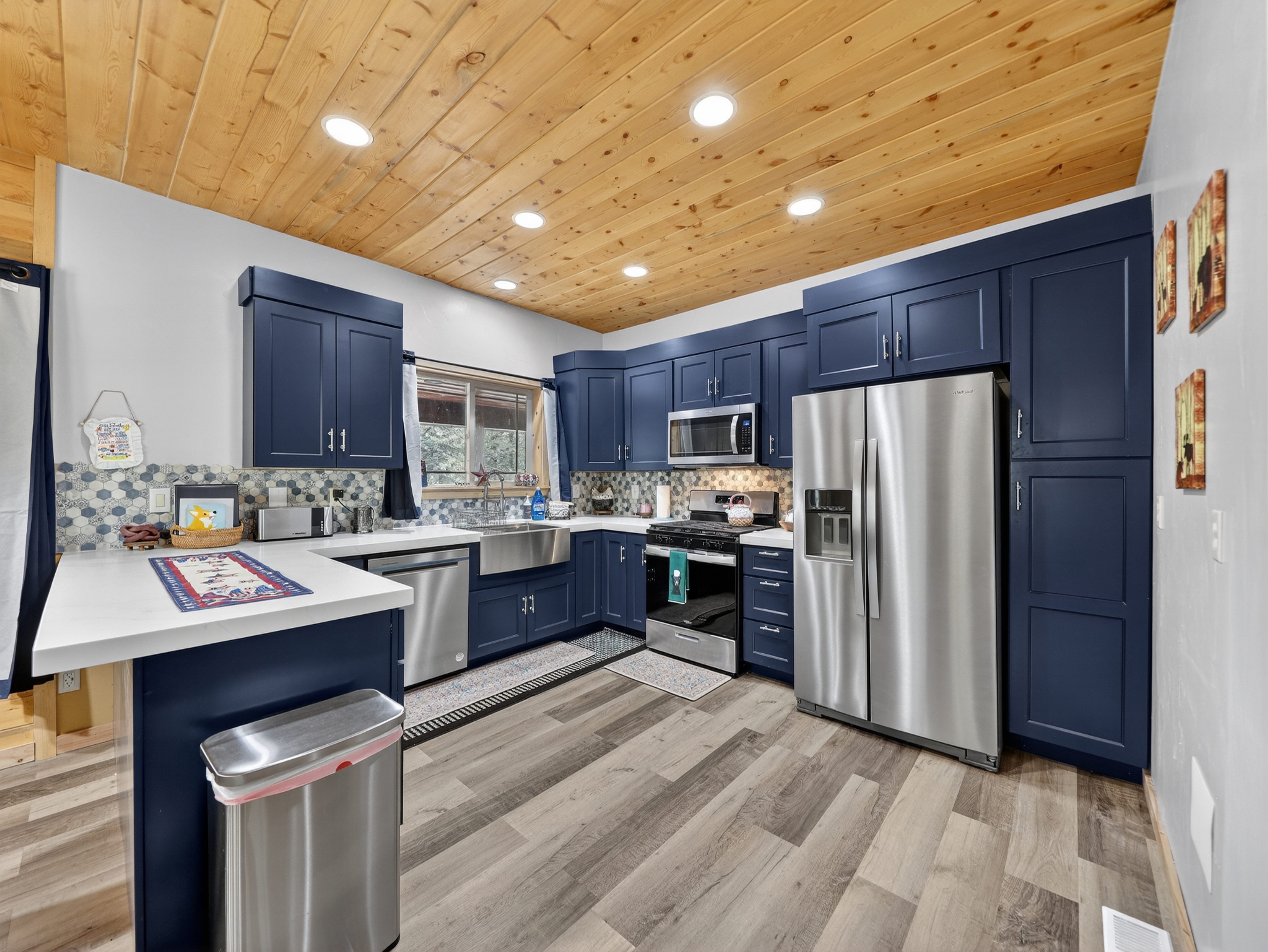 Step into your fully equipped modern kitchen with rich navy cabinetry, stainless appliances, and warm wood plank ceilings—your home base for meals and memories.