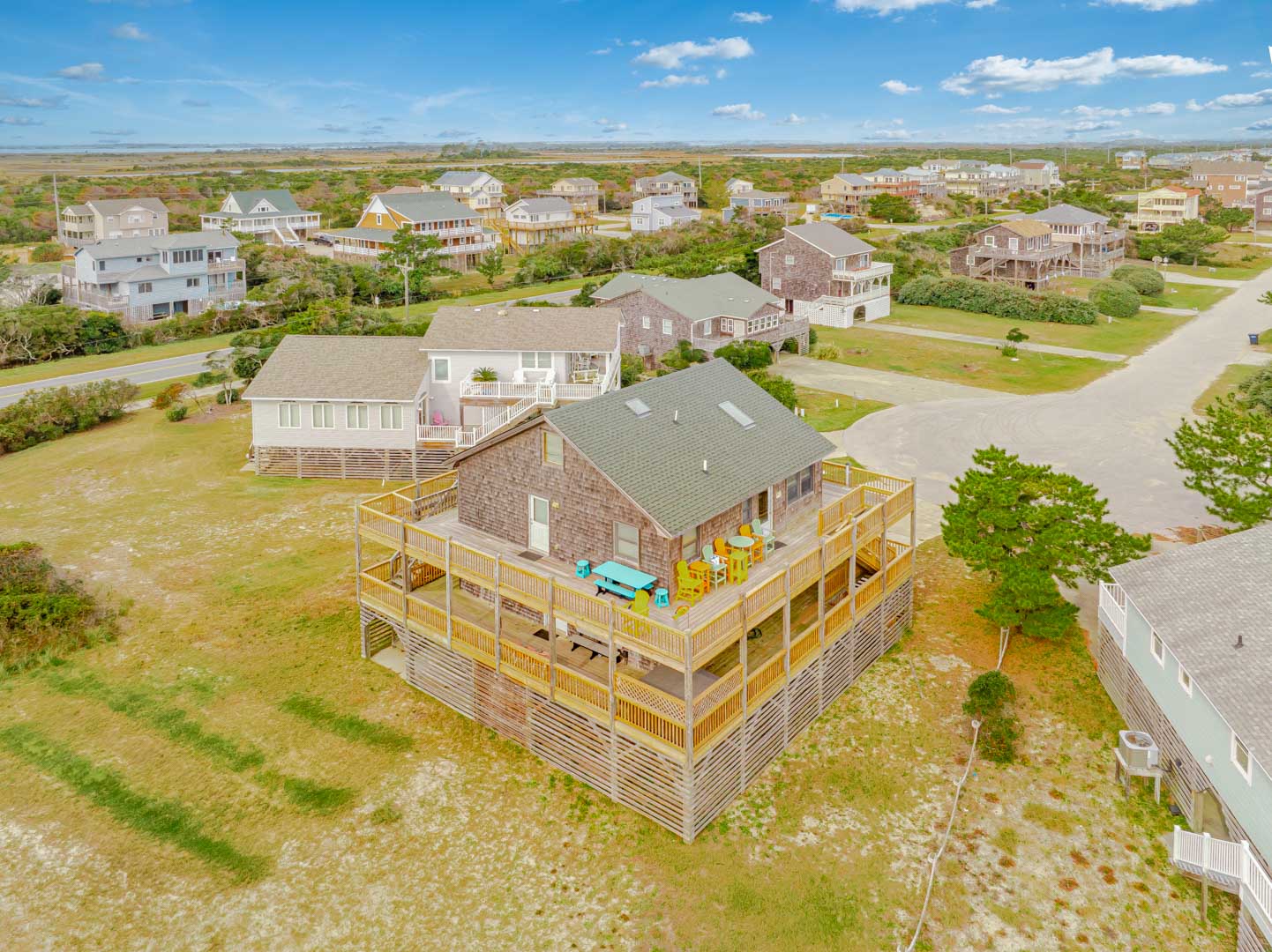 Aerial view of coastal vacation rental with expansive deck and hot tub, nestled in peaceful residential neighborhood.