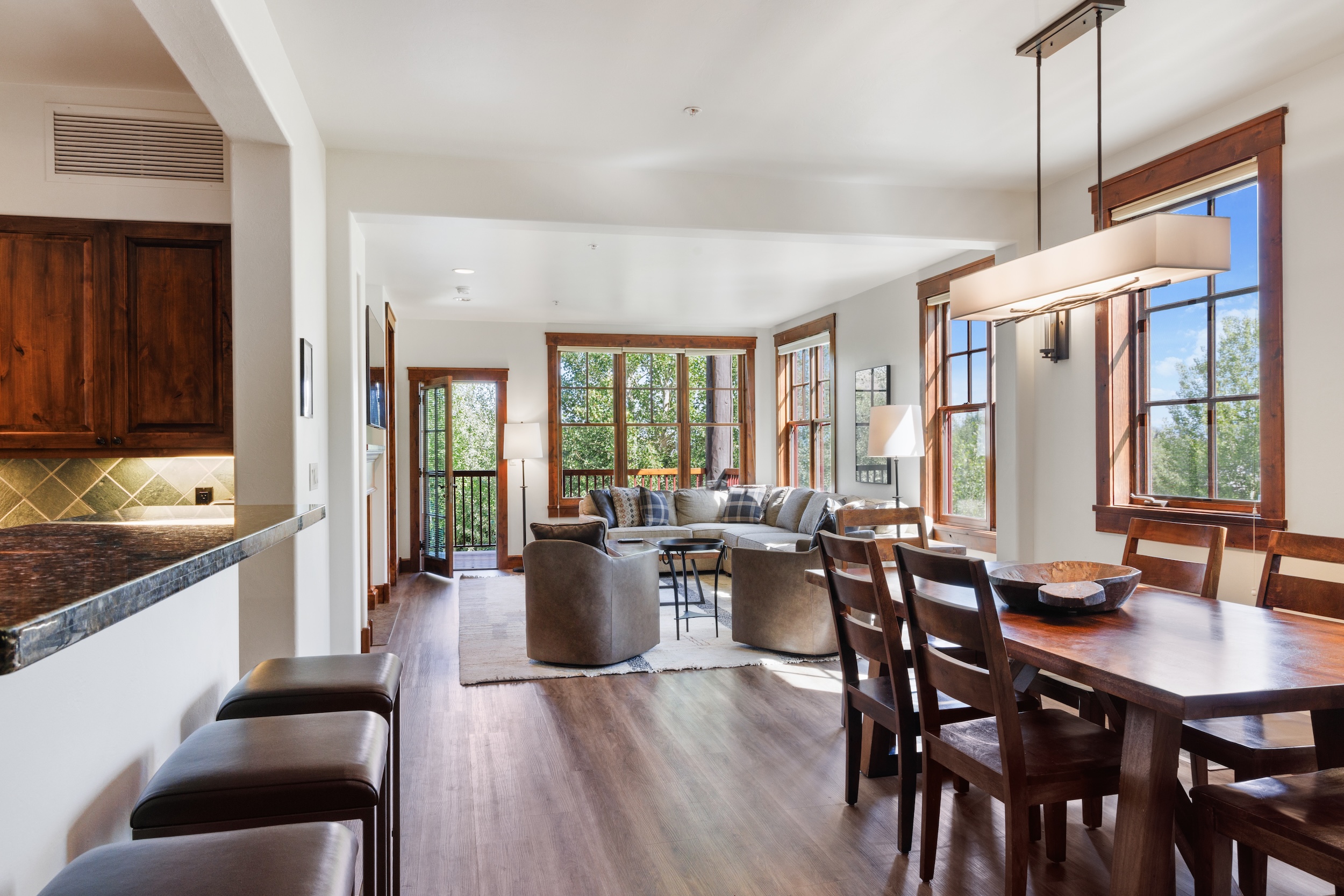 Bright and open with rich wood tones and sleek finishes. Sunlight streams through expansive windows, framing lush natural views. The living area and dining space invite you to relax and feel at home.