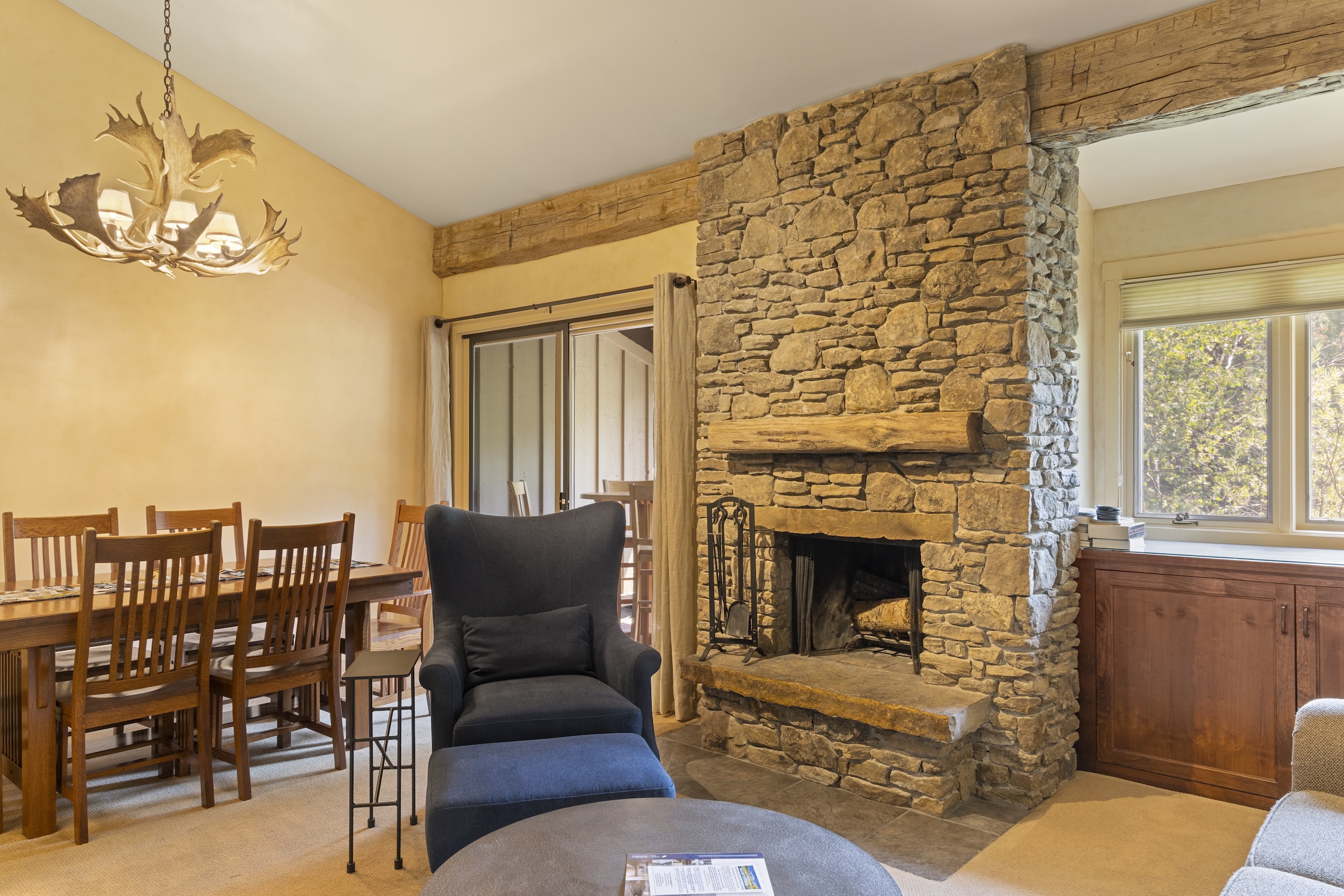 Settle in by your private stone fireplace with a warm fire crackling, while the rustic antler chandelier casts a gentle glow overhead. Sunlight streams through windows framing the treetops outside.