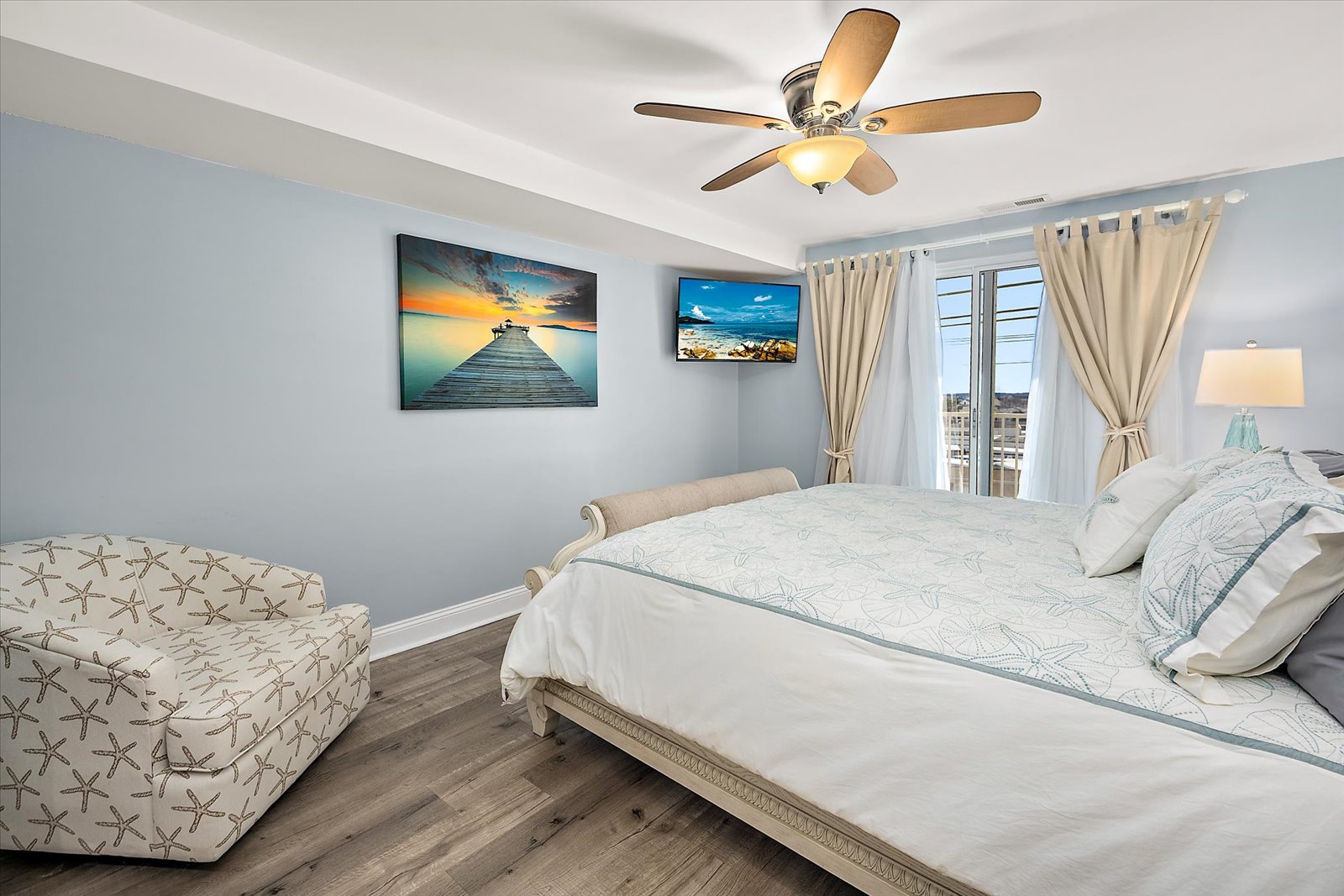 A bright and airy bedroom space complete with coastal artwork, a wall-mounted TV, and plenty of natural light.