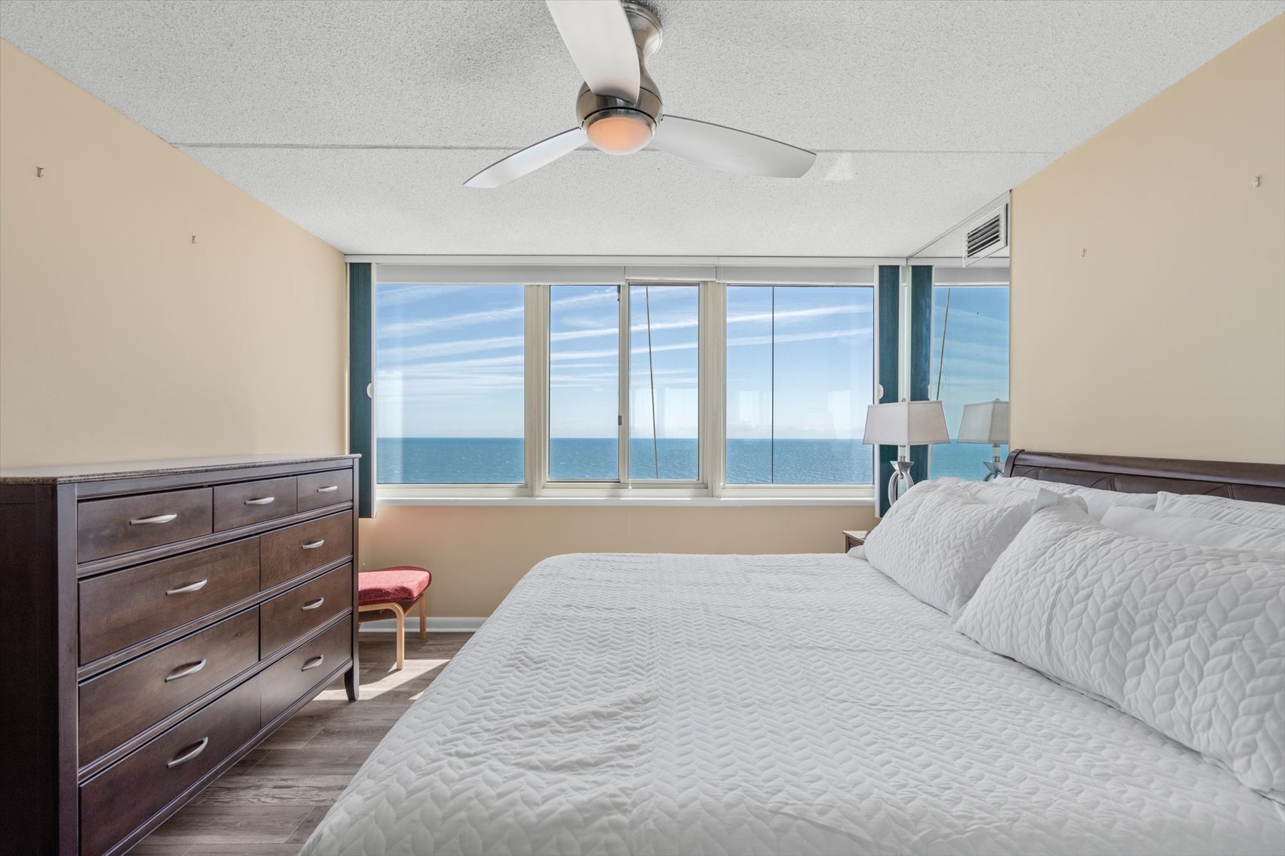 A master retreat complete with a plush bed, a large matching dresser, a ceiling fan, and panoramic ocean vistas.