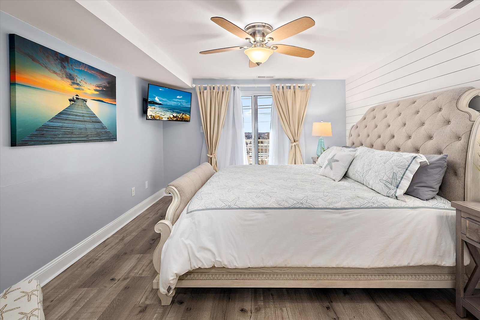 This comfortable bedroom offers a ceiling fan, flatscreen TV, and direct access toward the balcony glass doors.