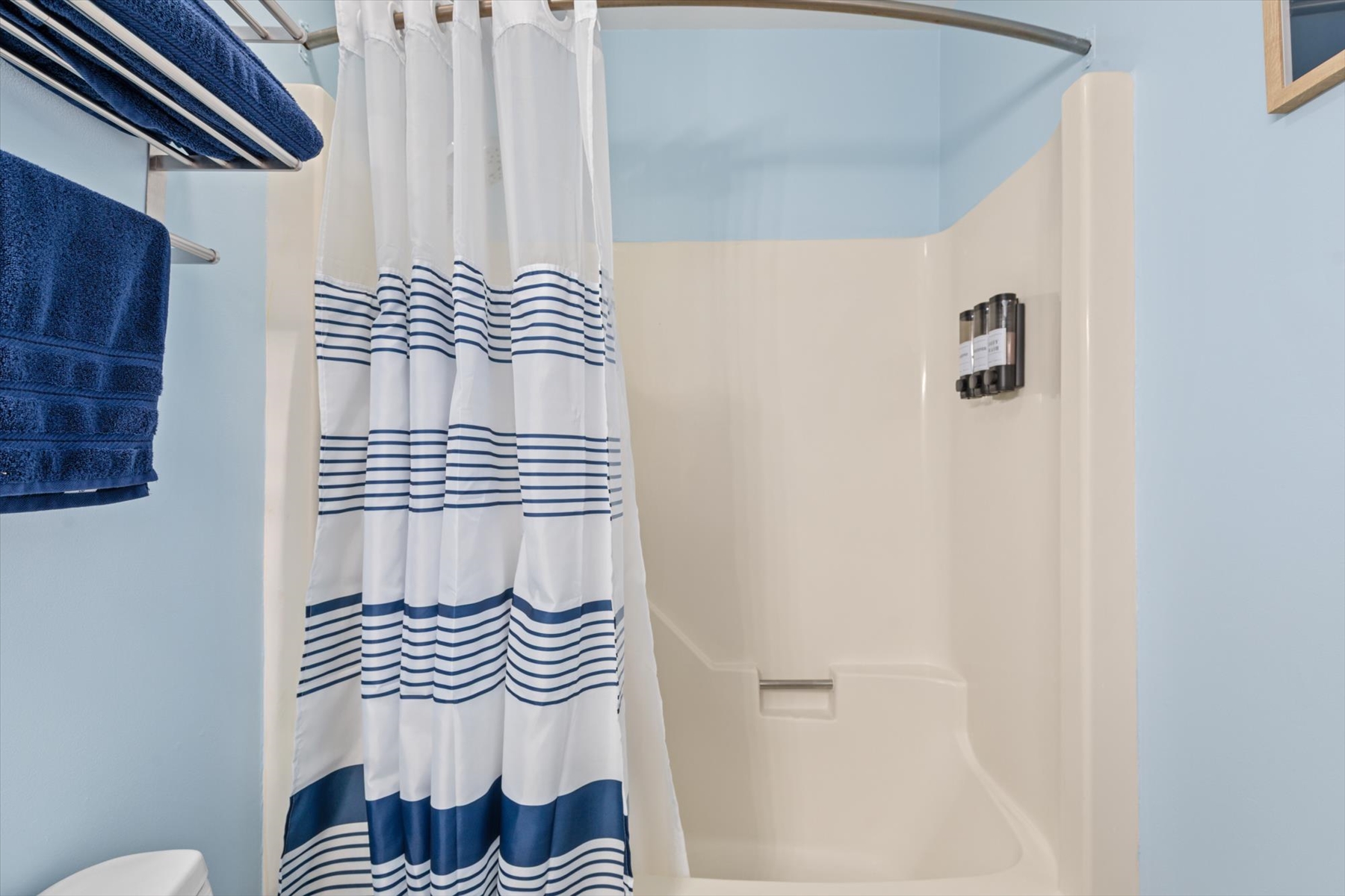 A closer look at the clean bathtub and shower combination, styled with a nautical blue-and-white striped curtain.