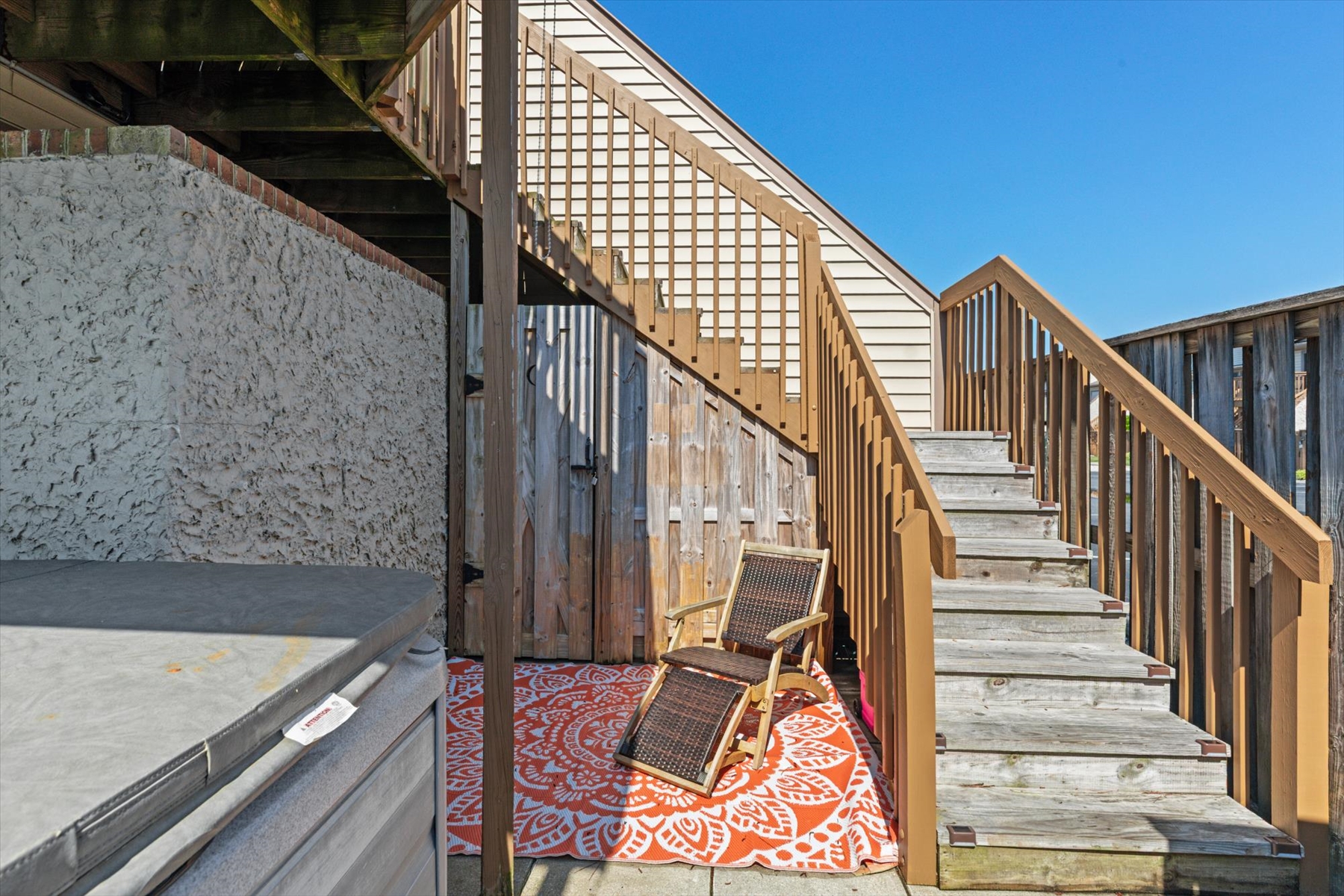 Step outside onto the lower concrete patio, offering a relaxing lounge chair on a decorative accent rug right next to the stairs.