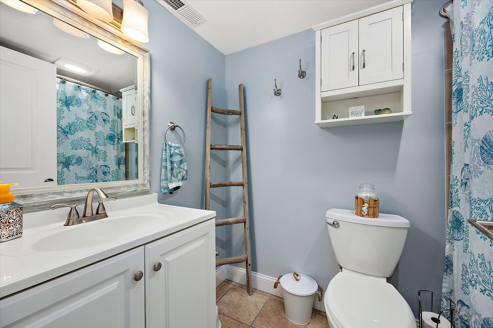 This well-appointed bathroom features a crisp white vanity, storage cabinets, and a decorative ladder towel rack.