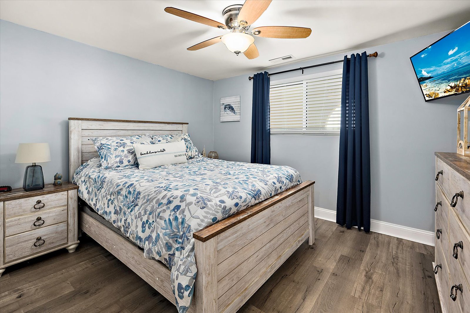 This charming second bedroom features coastal blue walls, a beautiful patterned quilt, and a cooling ceiling fan.