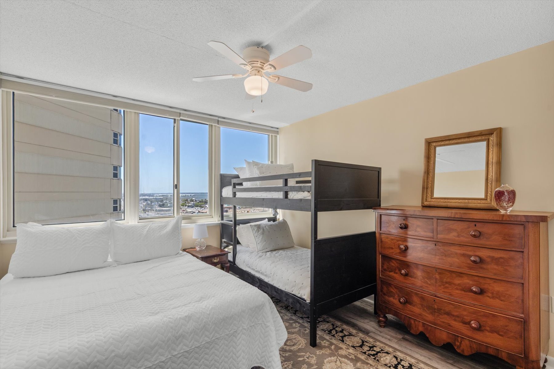 This bright, flexible sleeping space features a classic bunk bed configuration, a chest of drawers, and a ceiling fan.