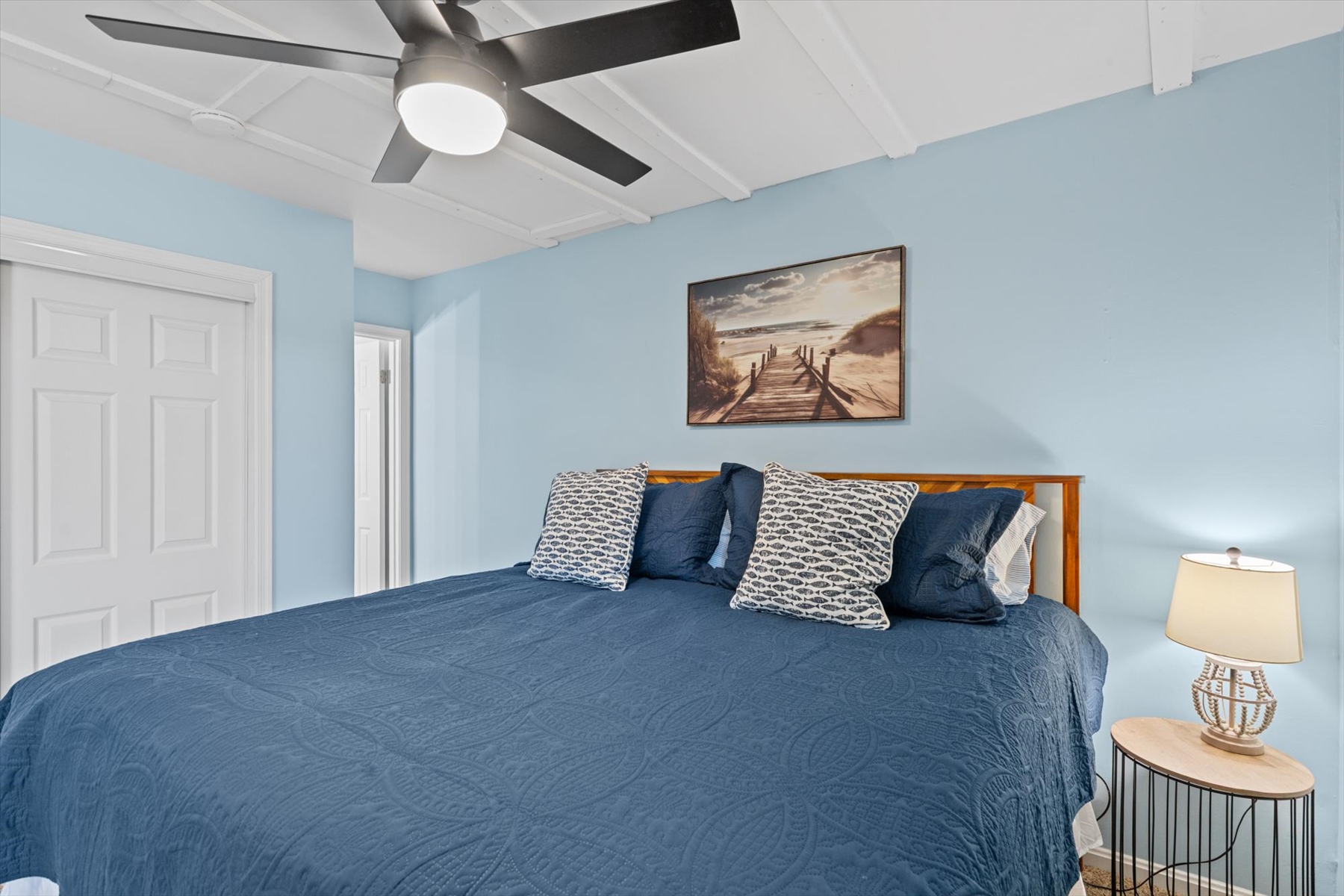 Rest easy in the primary bedroom, featuring a large bed with a deep blue coverlet, matching pillows, and calming light-blue walls.