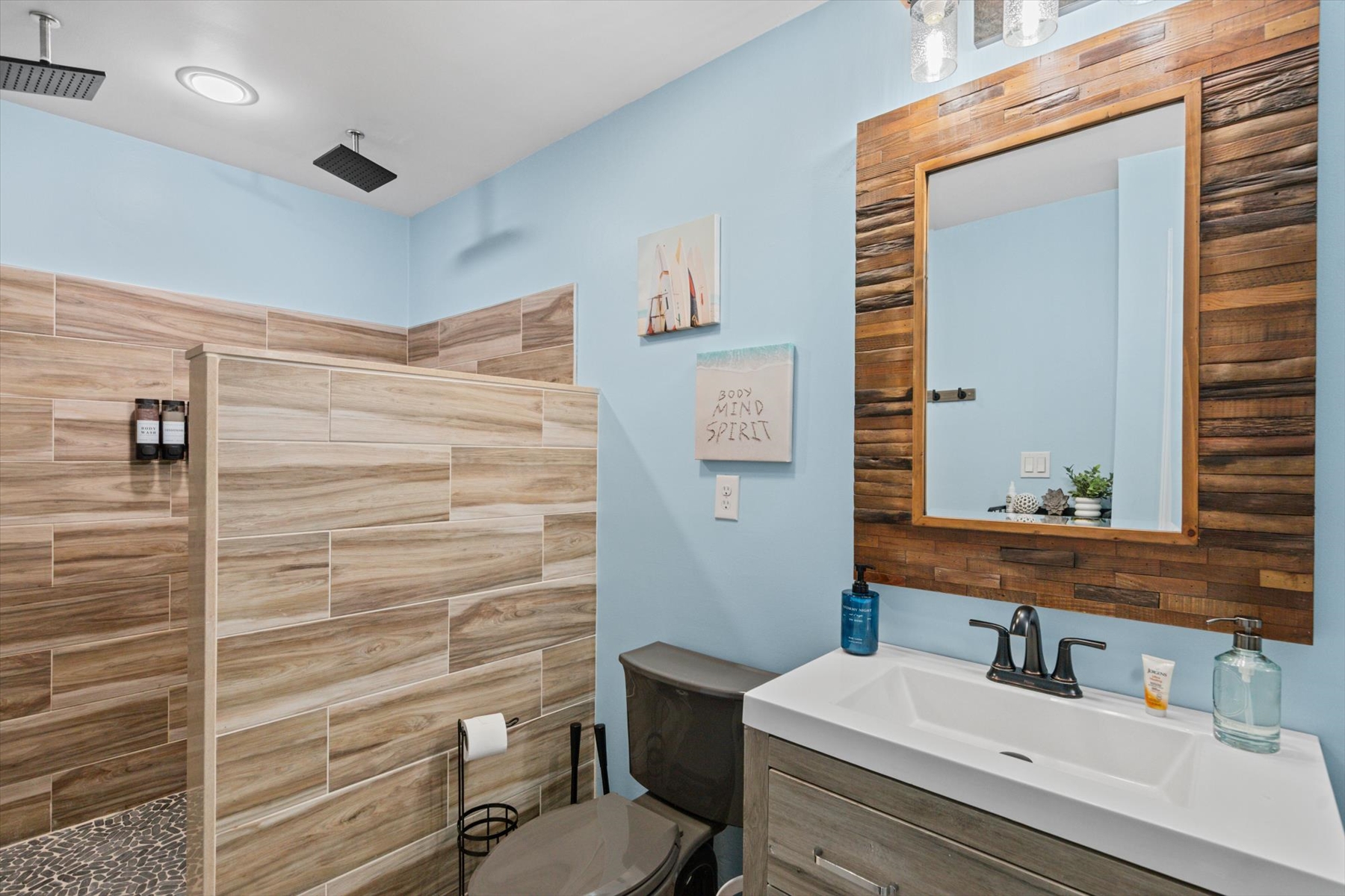 The second bathroom showcases a modern vanity with a beautiful rustic wood-framed mirror and a sleek, multi-toned tiled shower wall.