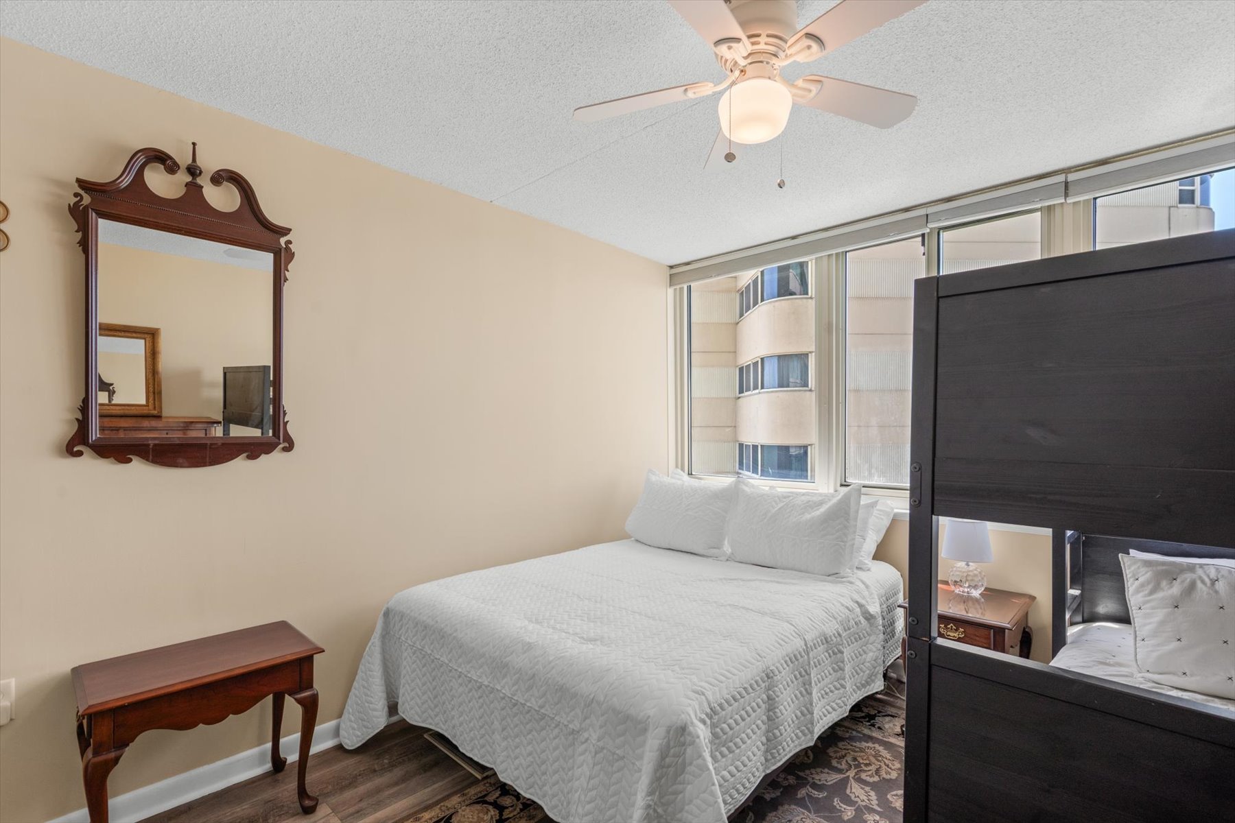 A cozy guest bedroom offering a restful setup with a cooling ceiling fan and a calm, sunny atmosphere.